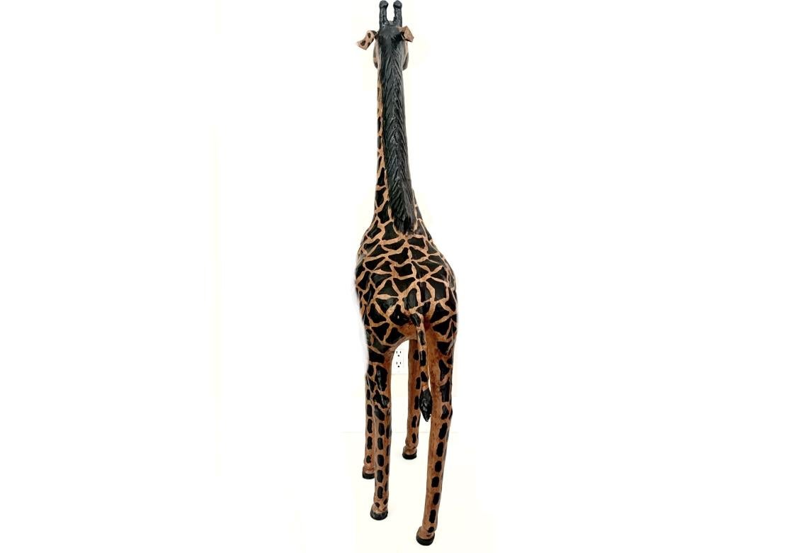 A nearly life-size baby giraffe leather wrapped sculpture with a patterned coat throughout, black carved mane, short hairy horns, elongated muzzle, black soulful eyes, long tail with tail tuft and resting upon long legs with black