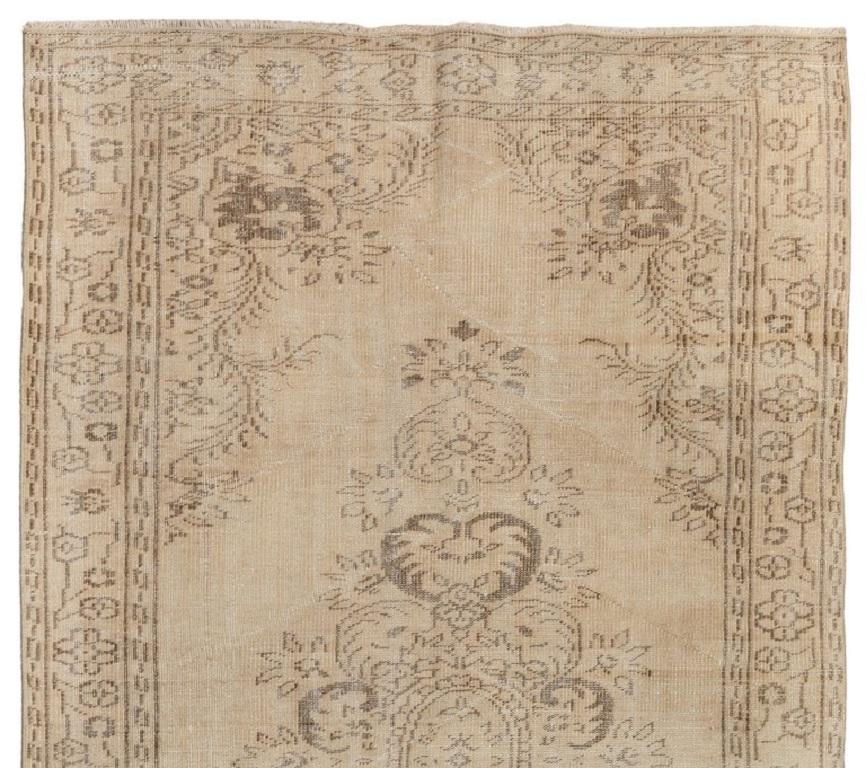 A finely hand-knotted vintage Turkish area from the 1960s with a delicate medallion made of scrolling vines at its centre as well as a border filled with stencil-like floral motifs, all against a sand-colored background. The rug has distressed low