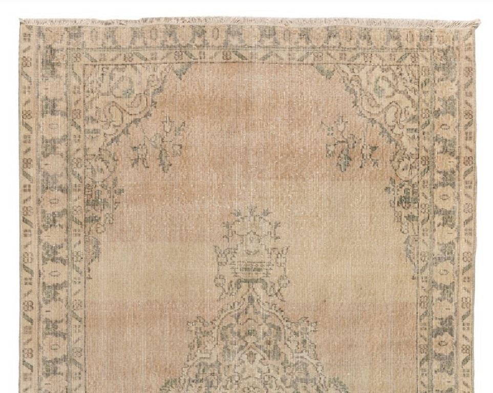 A vintage hand-knotted Turkish Oushak area rug from the 1960s with distressed low wile on cotton foundation. The rug has a central medallion on a sand-colored plain field framed by arabesque corner pieces and a three-layered border in soft, muted
