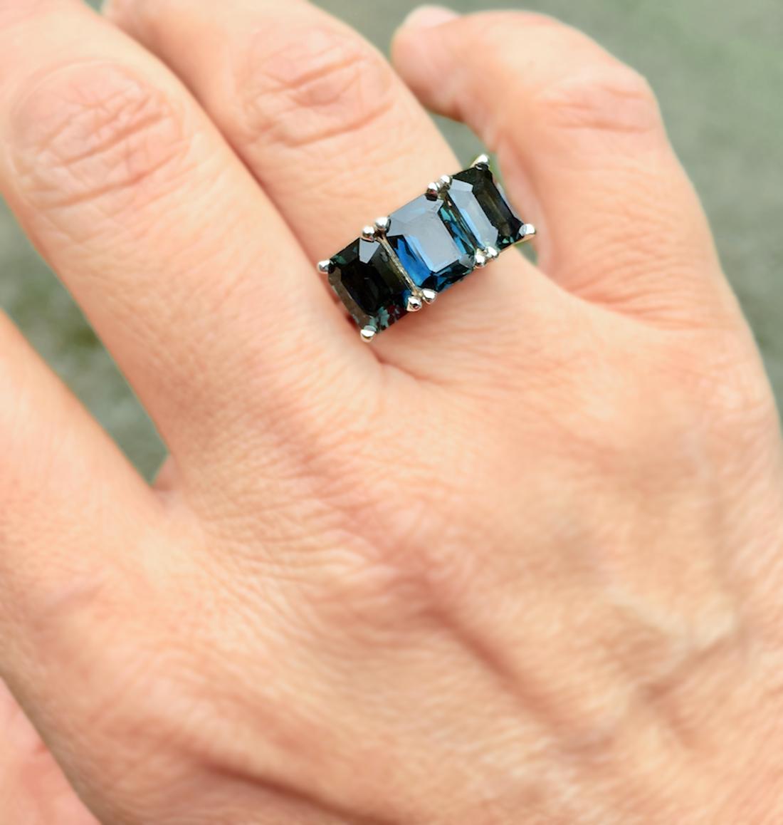 A three perfectly matched contemporary stylish Natural Sapphire three-stone wedding engagement ring unheated emerald-cut Sapphire, displaying a most unique dark teal, greenish blue color. All 3 Sapphires emerald cut with an approximate combined
