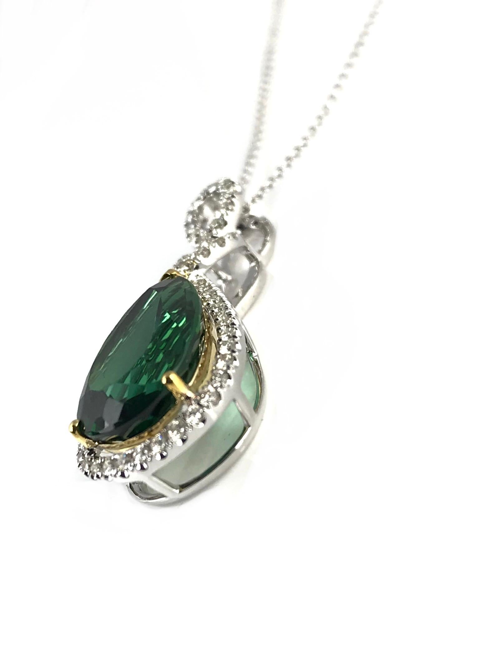 This elegant  pendant features a 5.50 carat pear shaped green tourmaline, inside of a delicate yellow gold setting, and surrounded by a halo of round natural diamonds. The body of the pendant hangs from a double layered bail, also decorated with