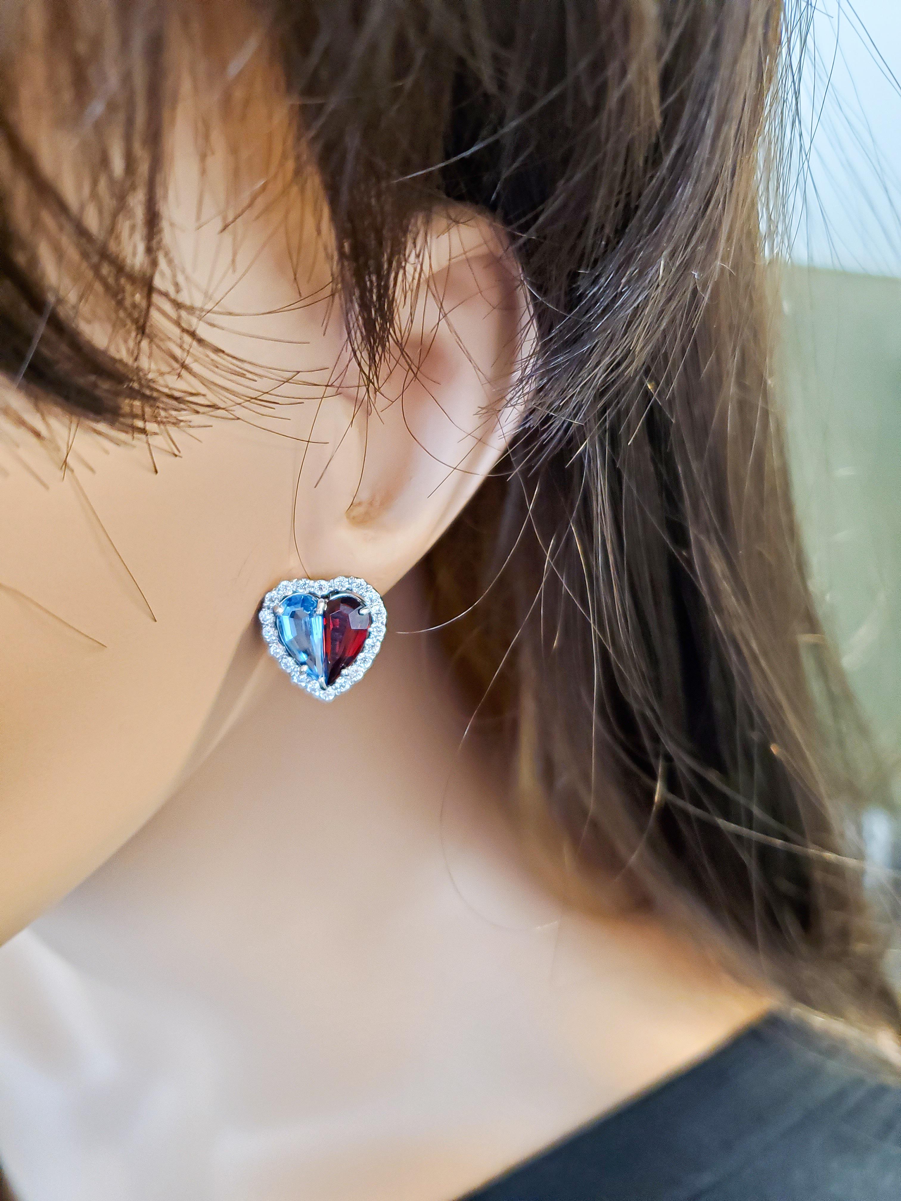 This lavish pair of earrings is designed in brightly polished 14 karat white gold and features expertly cut half-heart shaped Swiss blue topaz and dark red garnet stones in the center totaling 5.50 carats. These semi-precious colored gemstones are