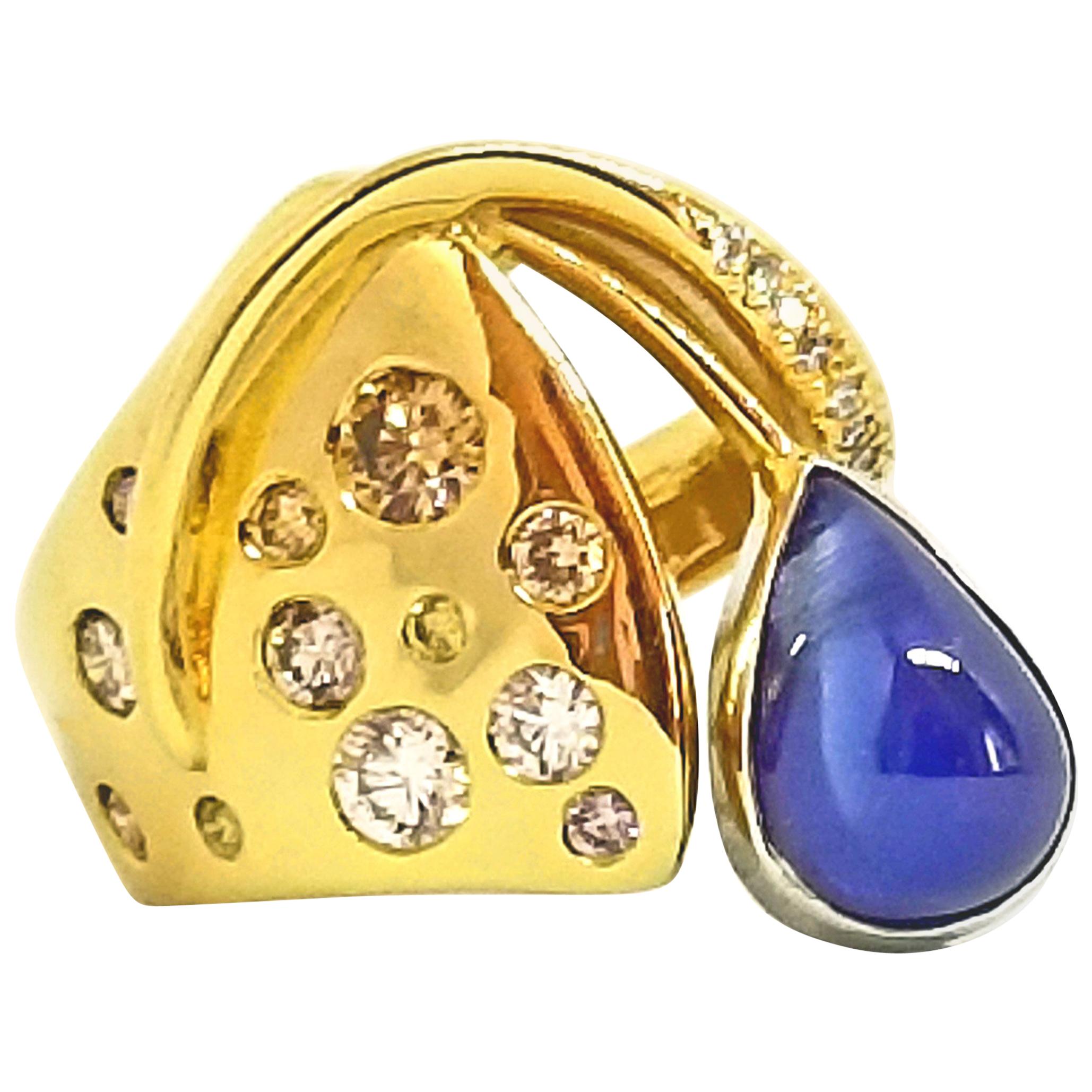 This one of a kind, artist designed and crafted Statement Ring features a 5.51 carat Sugarloaf Sapphire. The Tear Drop Shaped stone is a Translucent Medium Blue and is Bezel set in 18K White Gold. The Contemporary Asymmetric ring is Highly Polished