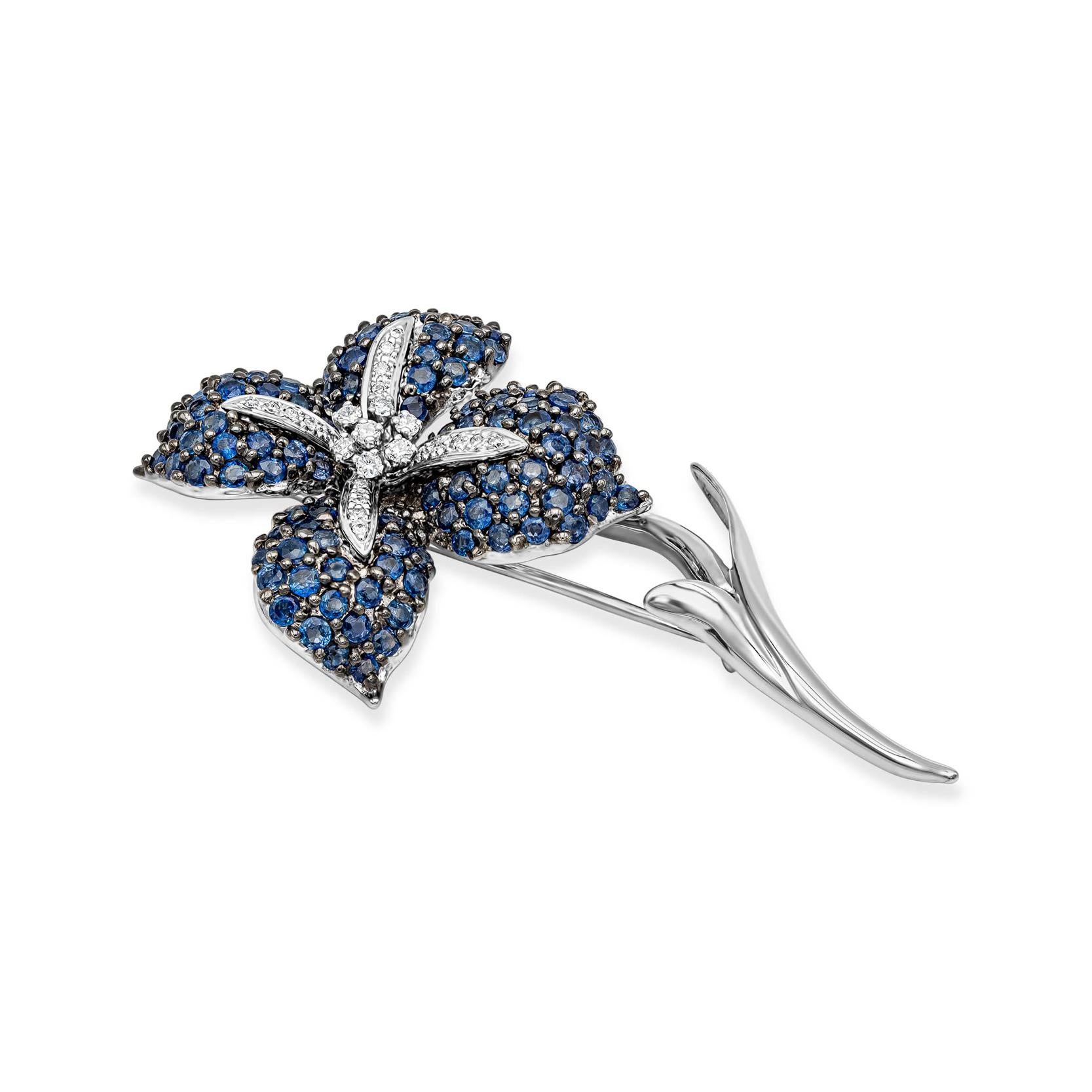 A beautiful pin showcasing 5.54 carats of blue sapphires and 0.36 carats of diamonds, set in a four petal flower design made in 18k white gold. 