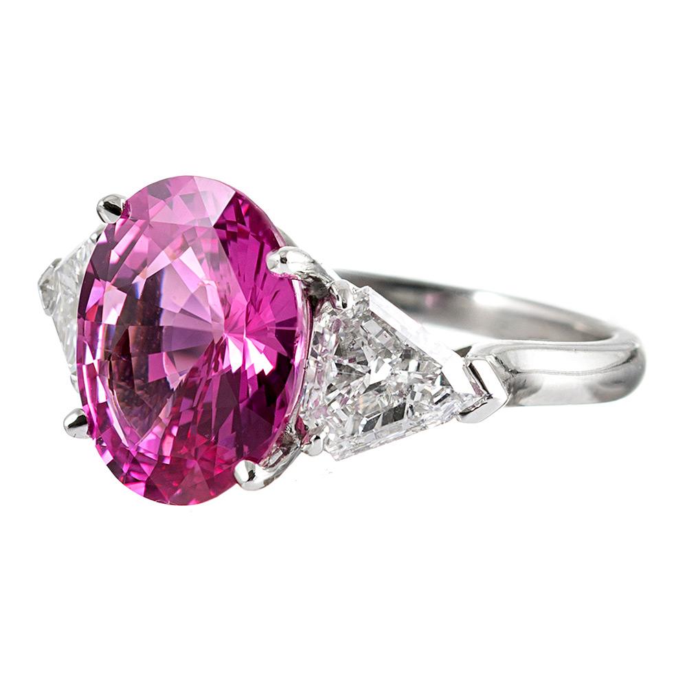 The center pink sapphire exhibits intense, truly gem fine properties, with exceptional color and brilliance. The major stone weighs 5.54 carats. It is flanked by a pair of shield-shaped white diamonds that one must look closely at to appreciate, as