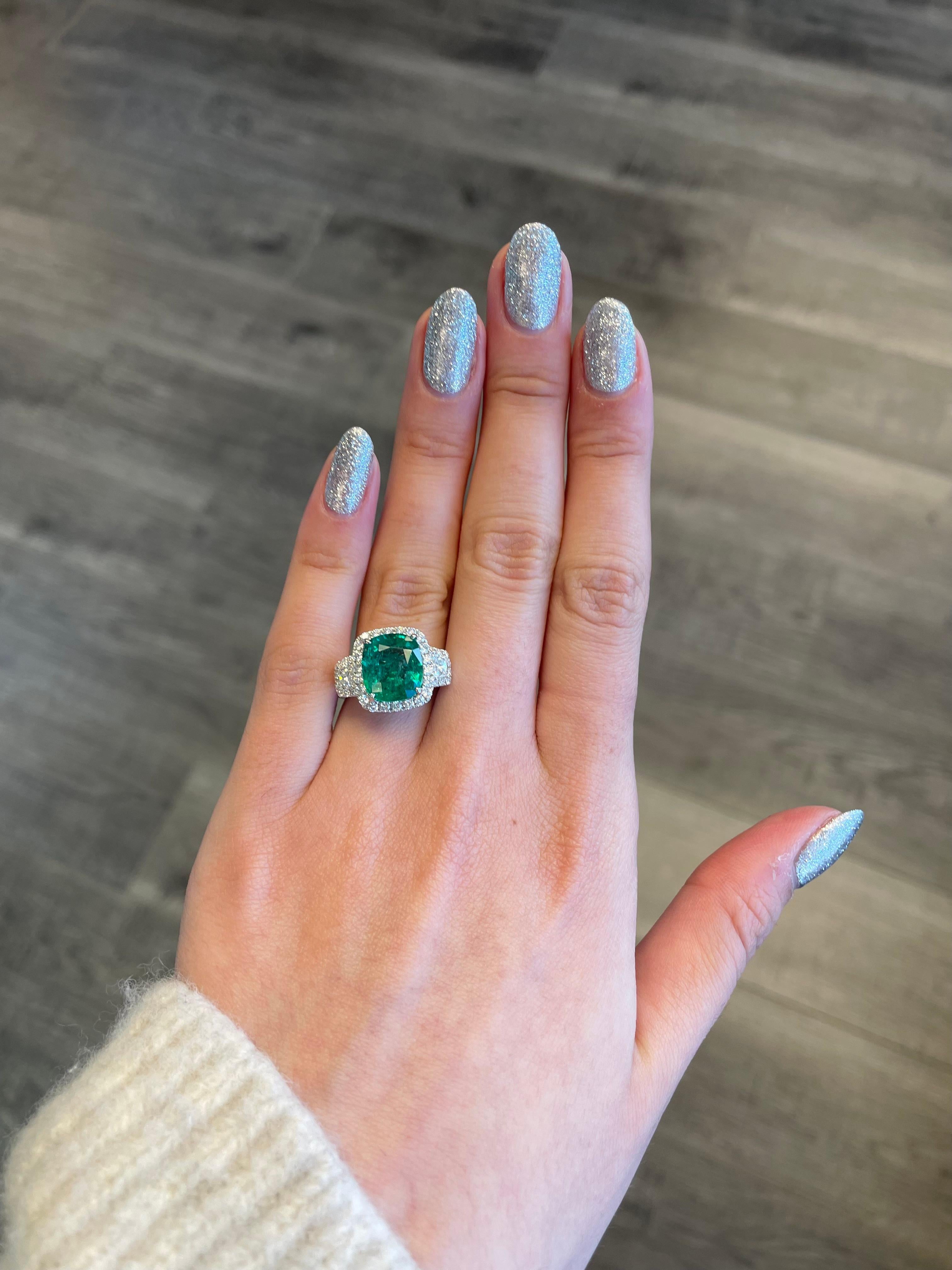 Stunning emerald and diamond three stone ring with halo. 
5.54 carats total gemstone weight.
4.23 carat cushion emerald, apx F2. 2 trapezoid with 58 round brilliant diamonds, 1.31 carats. Approximately G/H color and VS-SI clarity. 18k white gold,