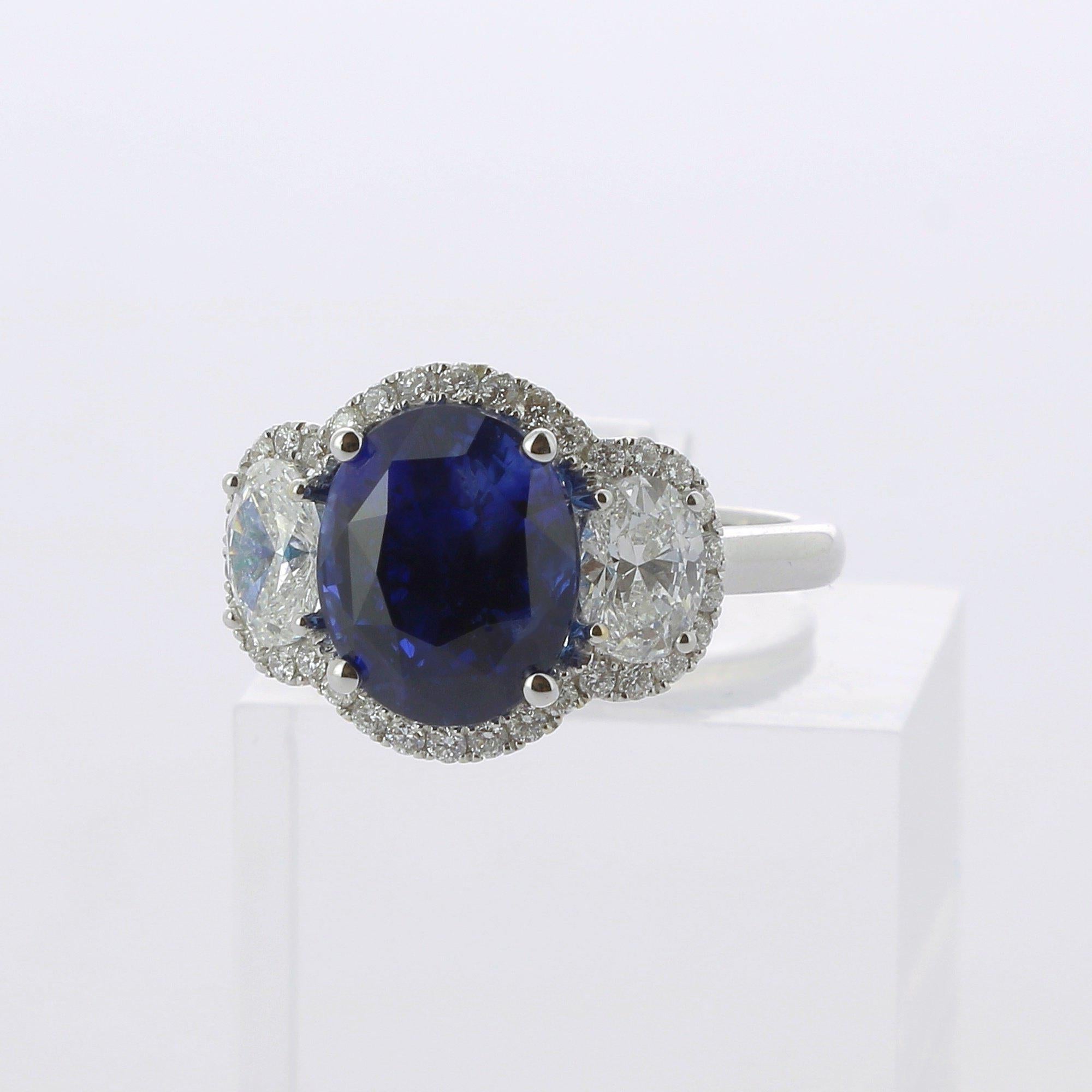 A Large and an amazing Oval Vivid Blue Sapphire Ring, flanked on each side by a single Oval Diamond and surround by a halo of Diamond weighing 0.29 Carats.
The total weight of the Sapphire is 5.56 Carats, the gemstone is certified as a 
 Vivid-Blue