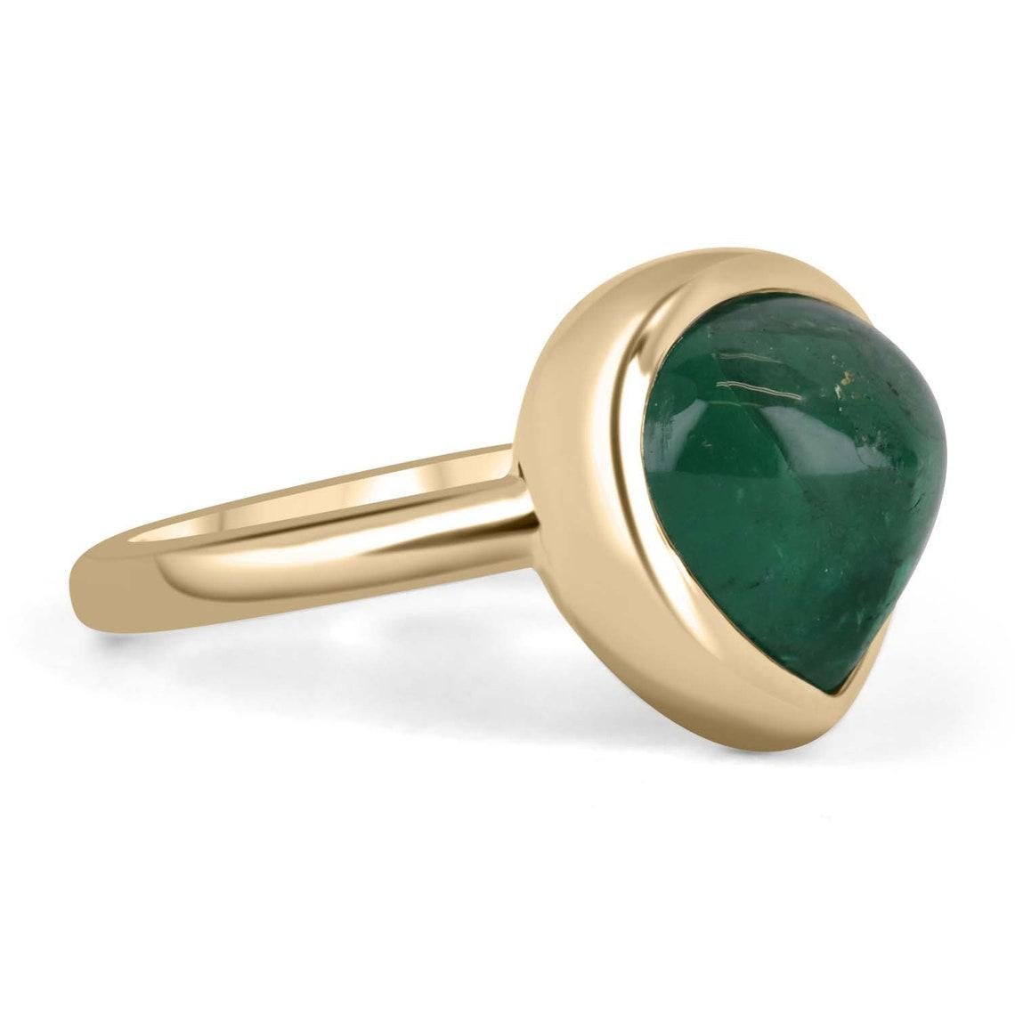 Displayed is a cabochon cut, chunky pear-shaped emerald bezel ring in 14K yellow gold. This gorgeous solitaire ring carries a full 5.56-carat emerald in a sleek bezel setting. The emerald has beautiful characteristics that will have you dazing into