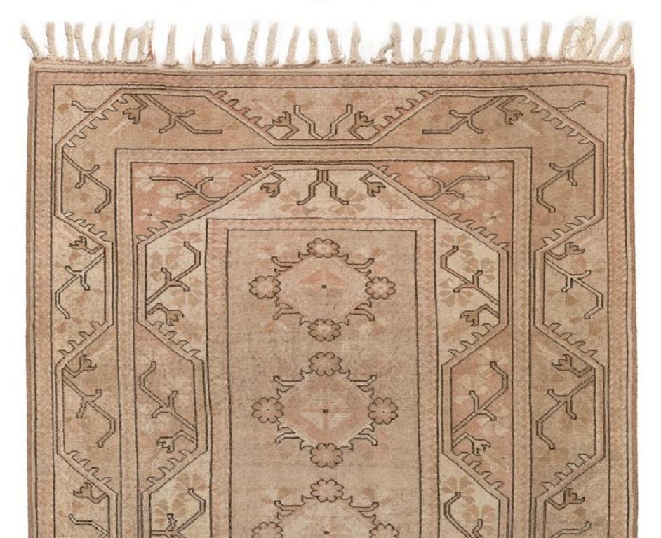 A finely hand-knotted Turkish area rug featuring geometric medallions, floral heads, large stylized serrated leaves placed in angular frames in beautiful gradations of soft, saturated pink and pinkish taupe colors. Measures: 5.5 x 8.3 ft

The rug is