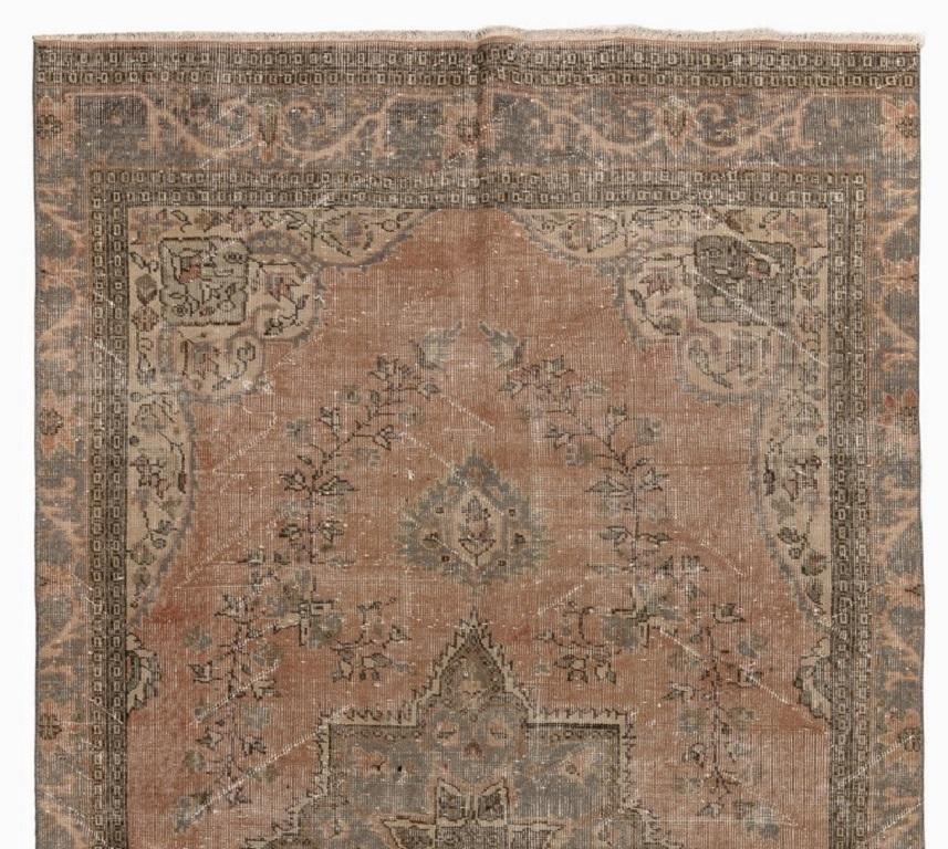 A finely hand-knotted vintage Turkish carpet from 1960s featuring a central medallion in gray surrounded all around by dainty scrolling floral vines against a faded rose background. The rug is made of low wool pile on cotton foundation. It is heavy