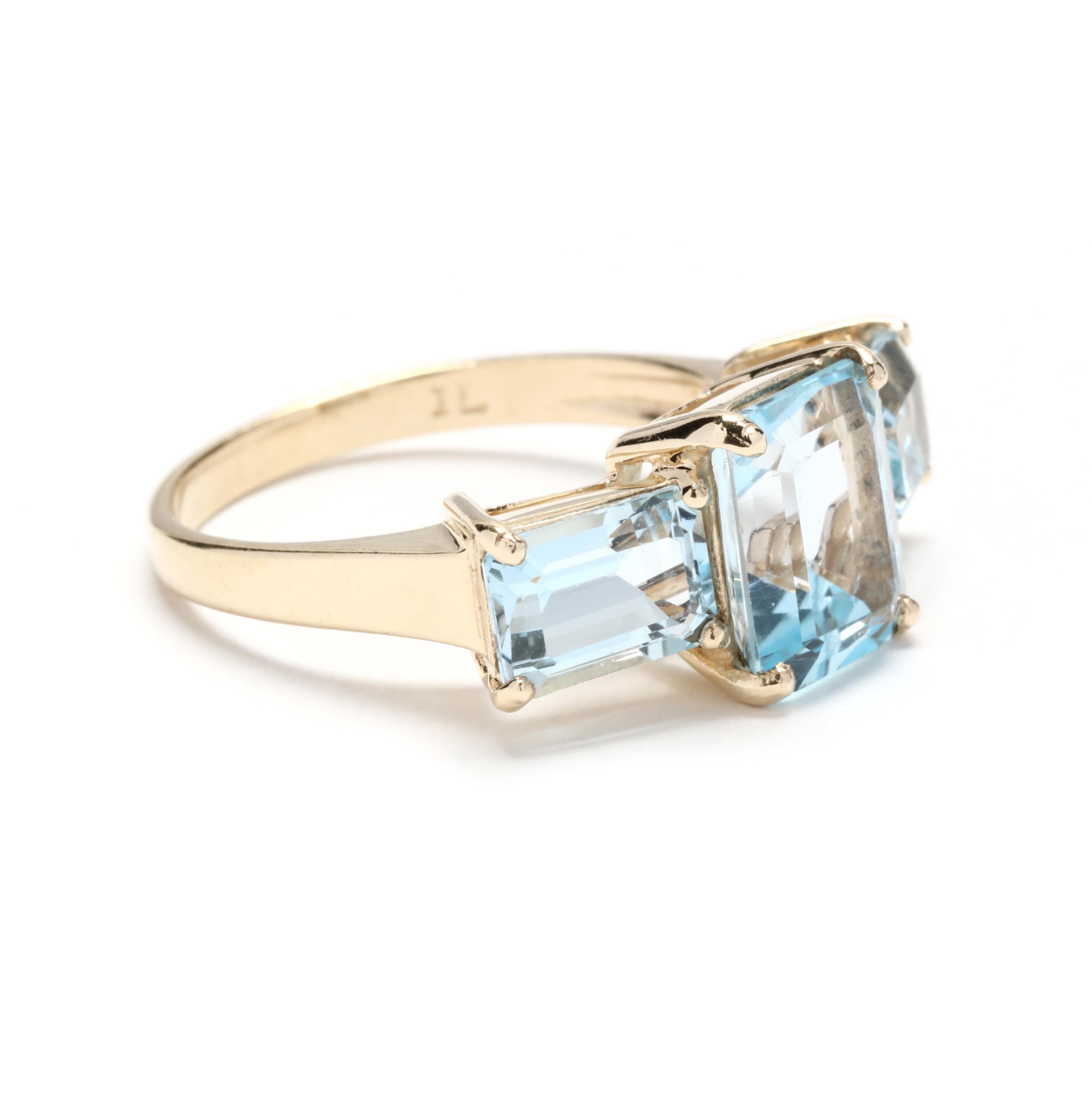 A vintage 10 karat yellow gold emerald cut blue topaz three stone ring. This December birthstone ring features a vertical prong set, emerald cut blue topaz center stone with horizontal emerald blue topaz stones on either side weighing approximately