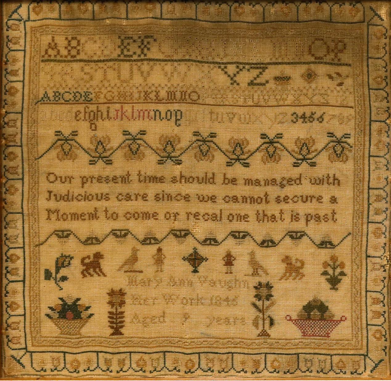 Un encantador sampler victoriano, bordado a mano por Mary Ann Vaughn. En hilo verde y amarillo se han cosido cuidadosamente a punto de cruz casillas del alfabeto, flores, animales y un verso. El muestrario ha sido bien presentado bajo cristal en un
