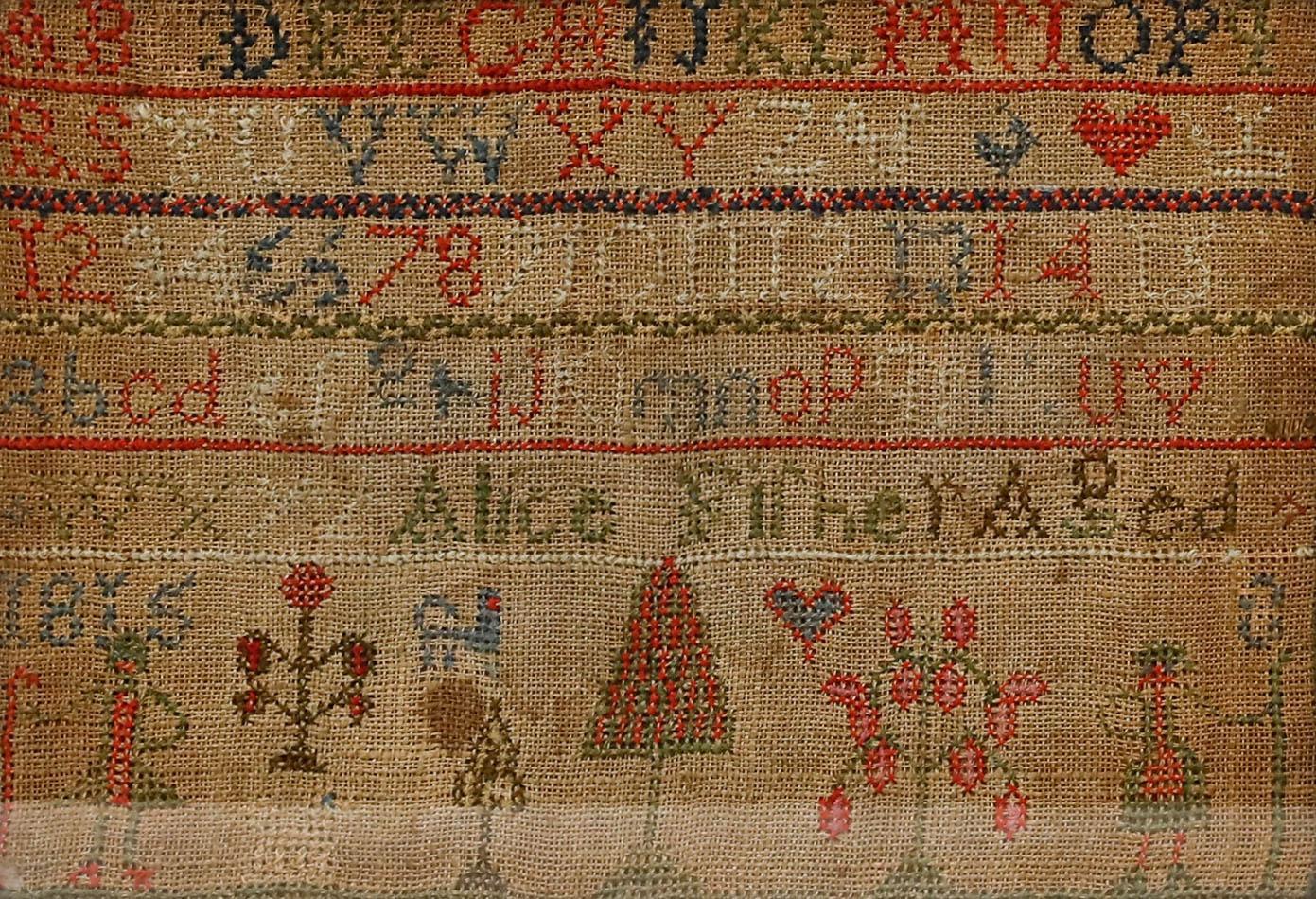 Un sampler géorgien coloré détaillant des cases de l'alphabet, des figures et des arbres. Créé par Alice Fisher, âgée de 9 ans, en 1815. Présenté dans un cadre rustique en bois derrière une vitre. Taille de l'image : 17,5 x 24,5 cm.