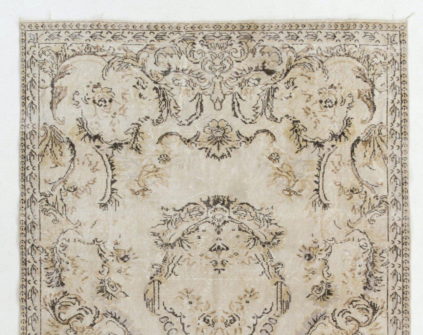 A vintage hand-knotted Turkish area rug from the 1960s that features a French-Aubusson inspired design of lush floral and leafy motifs made into stylized wreaths and cartouches arranged around the inner edges of the border, surrounding a central