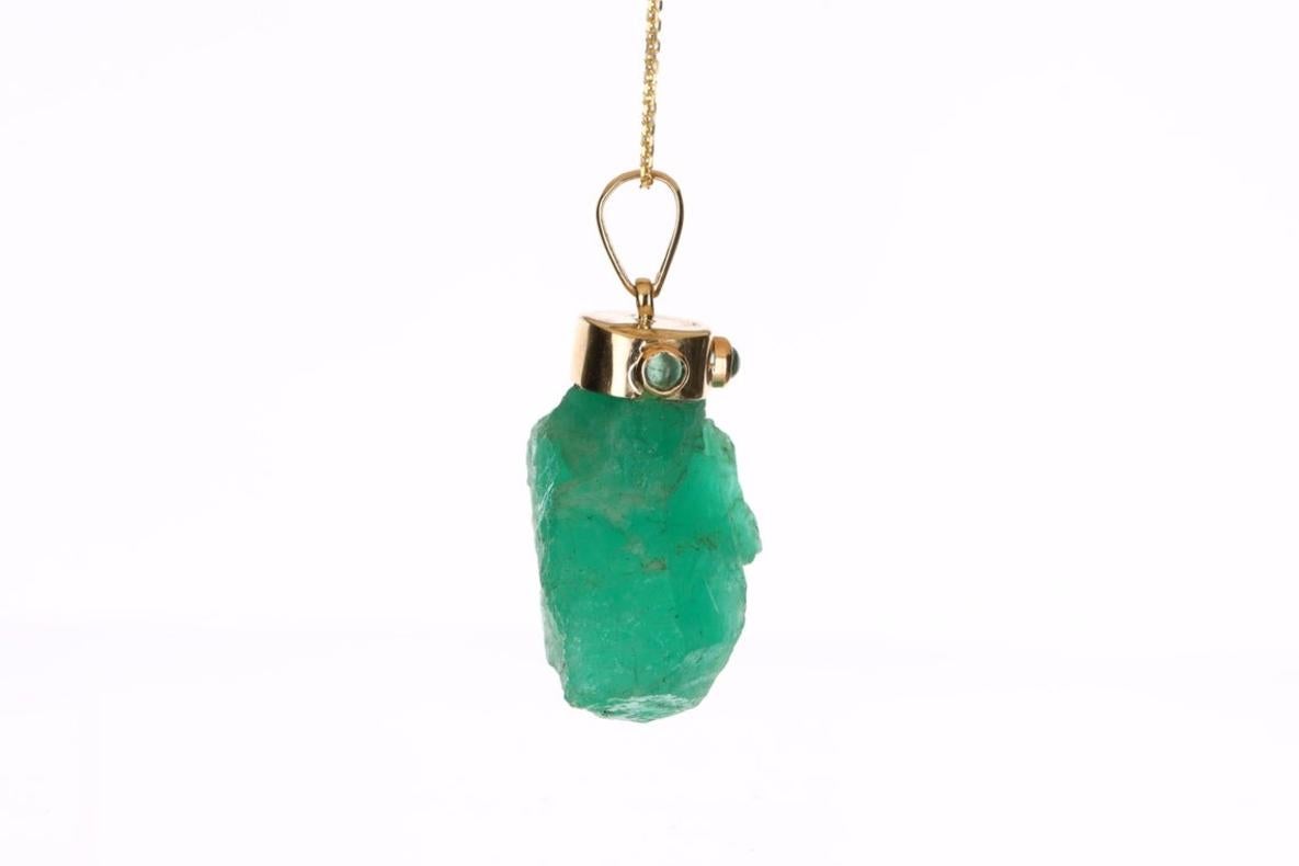 Showcased is a rare, rough emerald crystal pendant. 57 total carat weight of genuine, rough, Colombian emerald crystal is perfectly capped by smooth yellow gold and cabochon emerald bezel. The piece is semi-transparent and has a rich green color