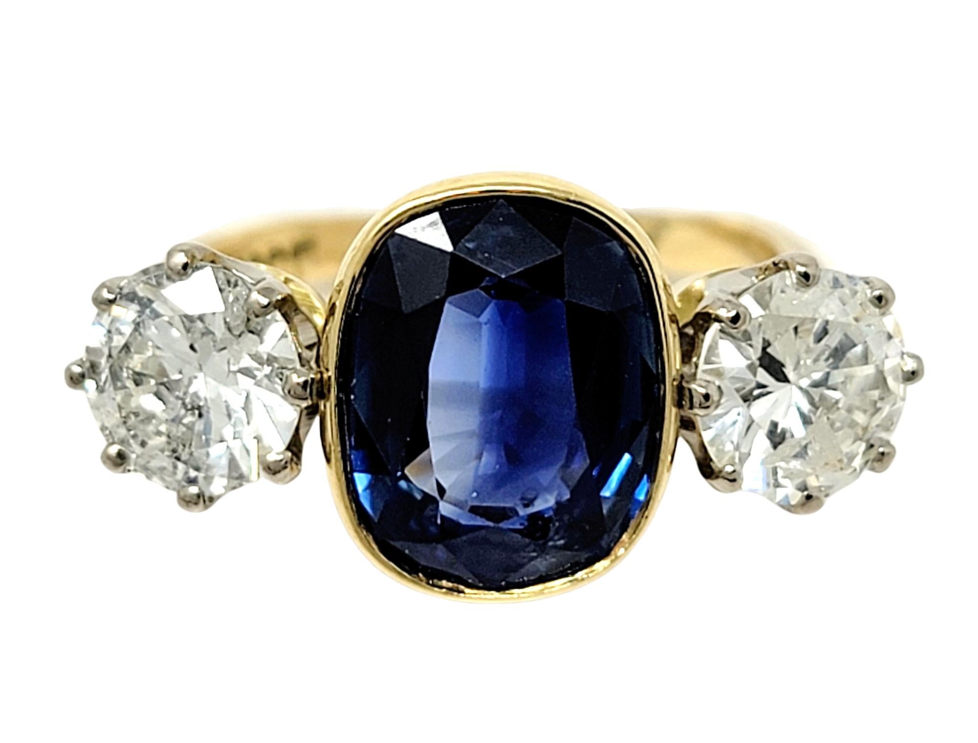 Ring size: 5.75

Simply stunning three stone sapphire and diamond ring. A modernized take on the classic three stone ring, this incredible piece fills the finger with sparkle. A cushion cut bezel set brilliant blue sapphire stone sits at the center,