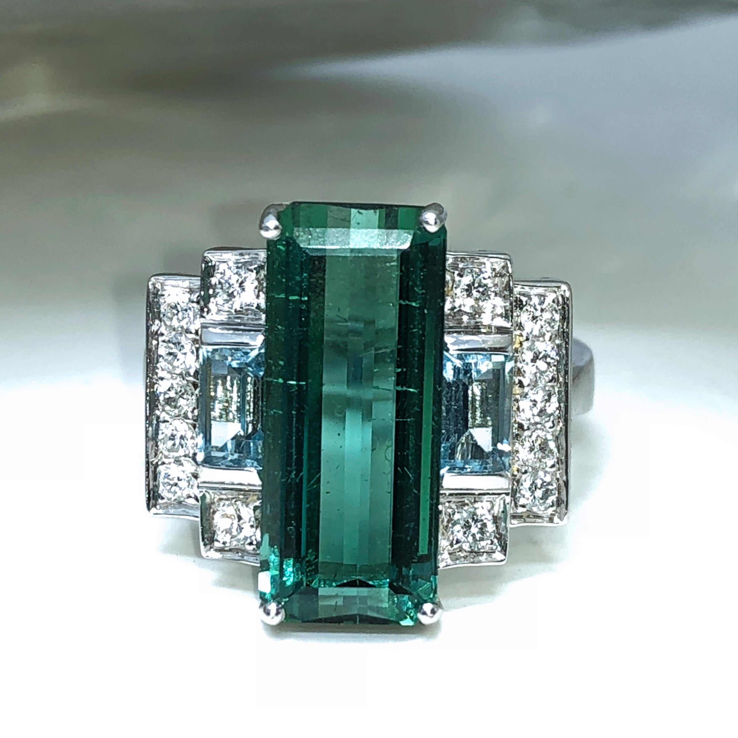 One-of-a-kind Cocktail Ring featuring an exceptional 5.75 Carat Baguette Cut Peacock Blue Natural Tourmaline surrounded by two Baguette Cut Aquamarine(0.84 Carat) in a White Diamond(0.29 Carat) 18Kt White Gold setting. In a fitted leather burgundy