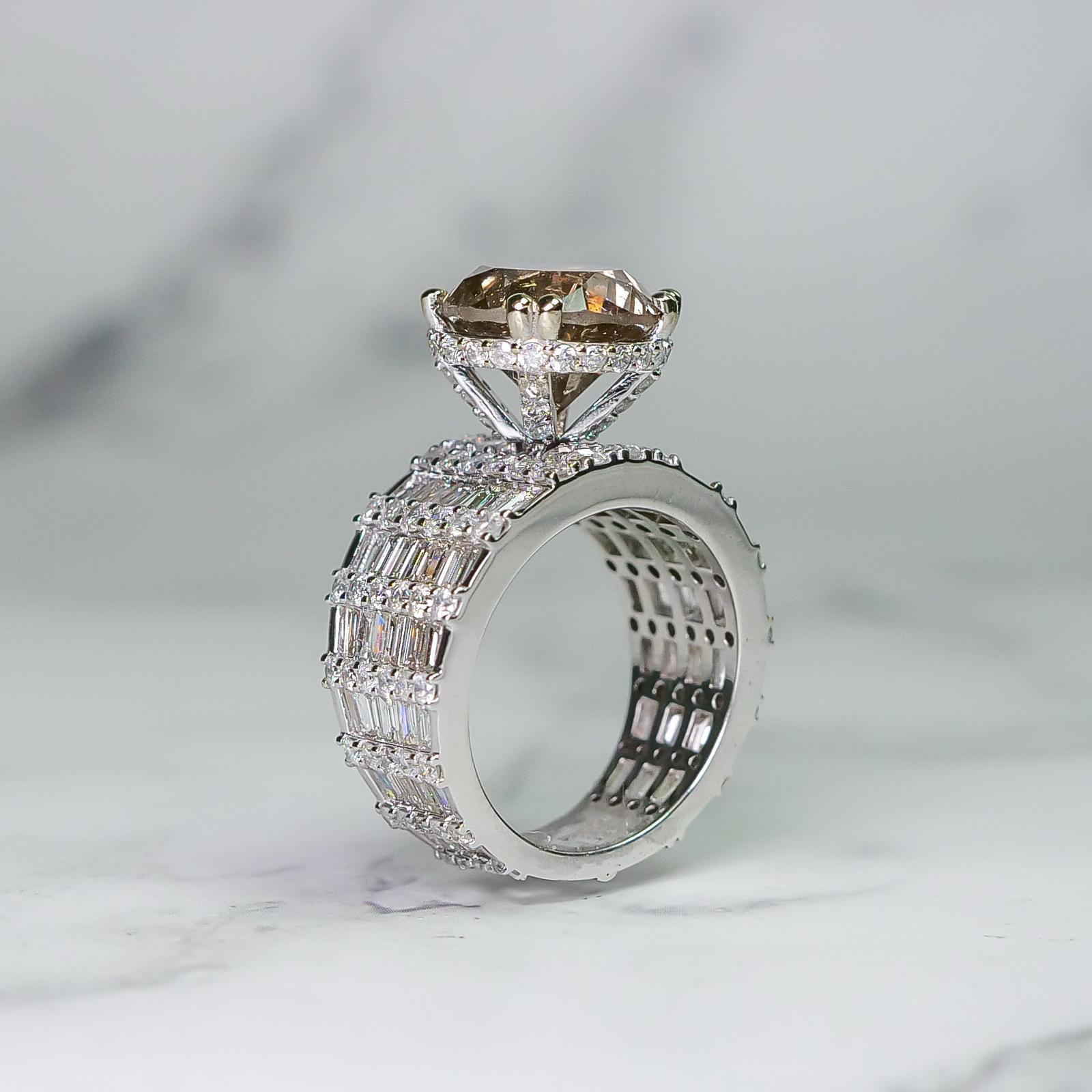 Este impresionante anillo de diamantes presenta una gran y brillante piedra central de diamante champán talla brillante de 5,75 ct rodeada por una banda de intrincados diamantes talla brillante y baguette de 3,92 ct en forma de banda. 

El anillo