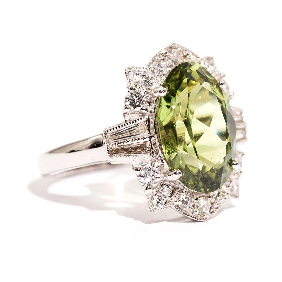 Forged in platinum is this wonderous ring that features a breath-taking 5.76 carat oval natural sapphire of a captivating bright yellowish-green colour encompassed with an alluring border of sparkling white round brilliant cut and baguette cut