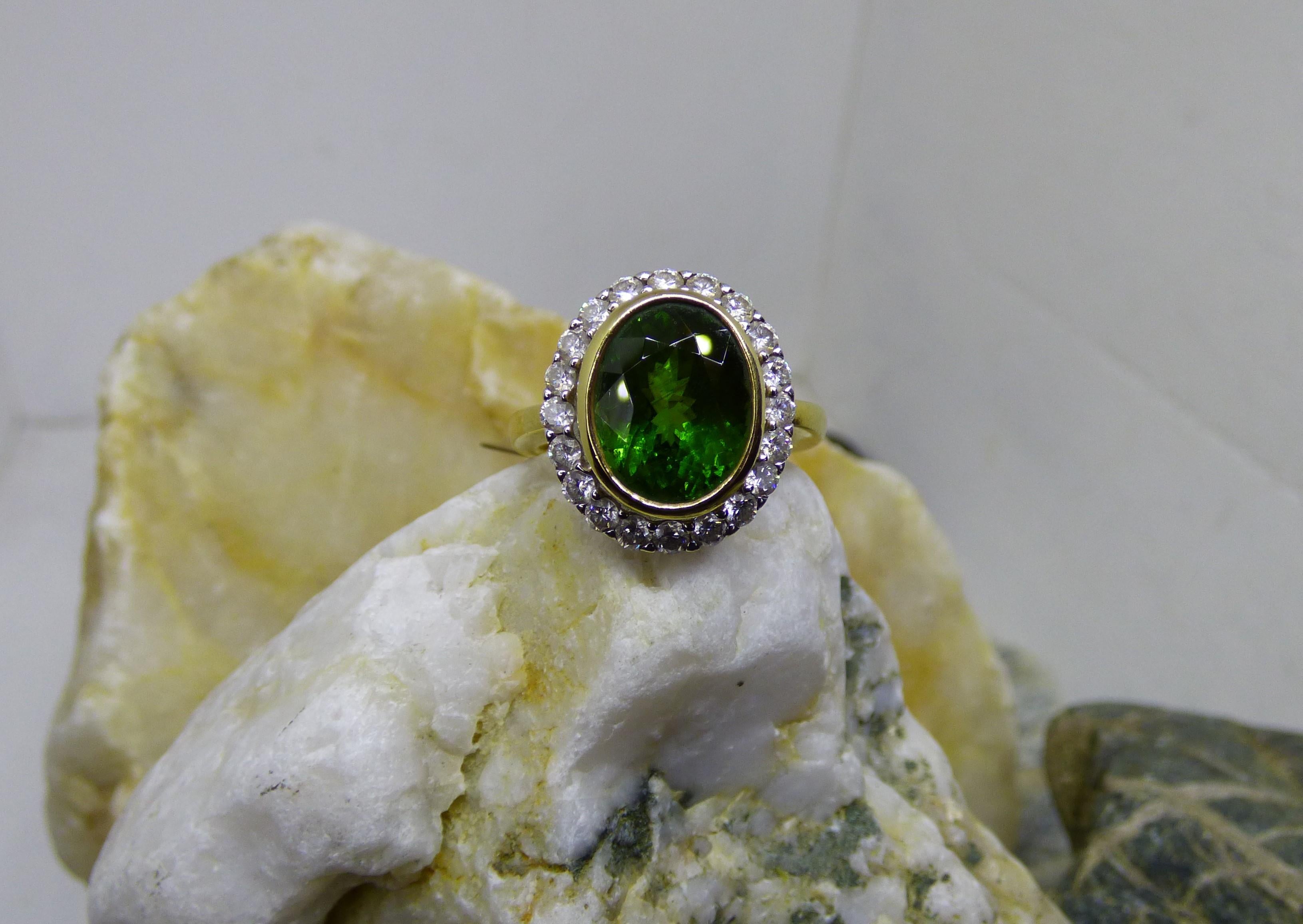 Ein grüner Turmalin, der hell und farbenfroh leuchtet.  Der facettierte ovale Turmalin hat 5,77ct. Der Turmalin ist von 20 Diamanten mit einem Gesamtgewicht von 0,85ct umgeben.  Der Ring ist handgefertigt aus 18 Karat Gelbgold und die Diamanten sind