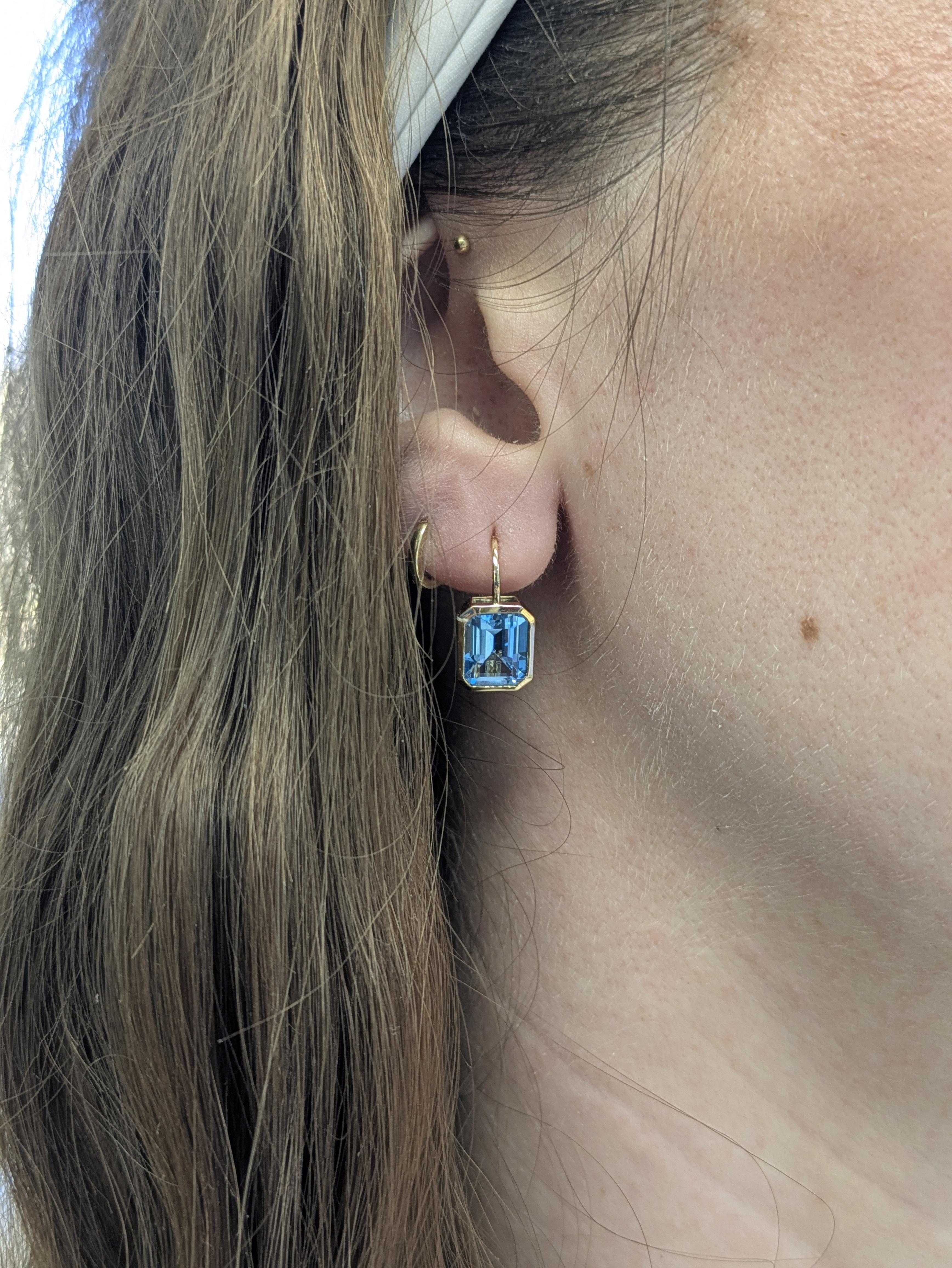 Diese Ohrringe aus brasilianischem himmelblauem Topas (5,7 Karat) strahlen eine ruhige Brillanz aus. Die Steine im Smaragdschliff sind 9x7 mm groß und in massivem 14-karätigem Gelbgold gefasst. Eine zeitlose Mischung aus Klarheit, Farbe und