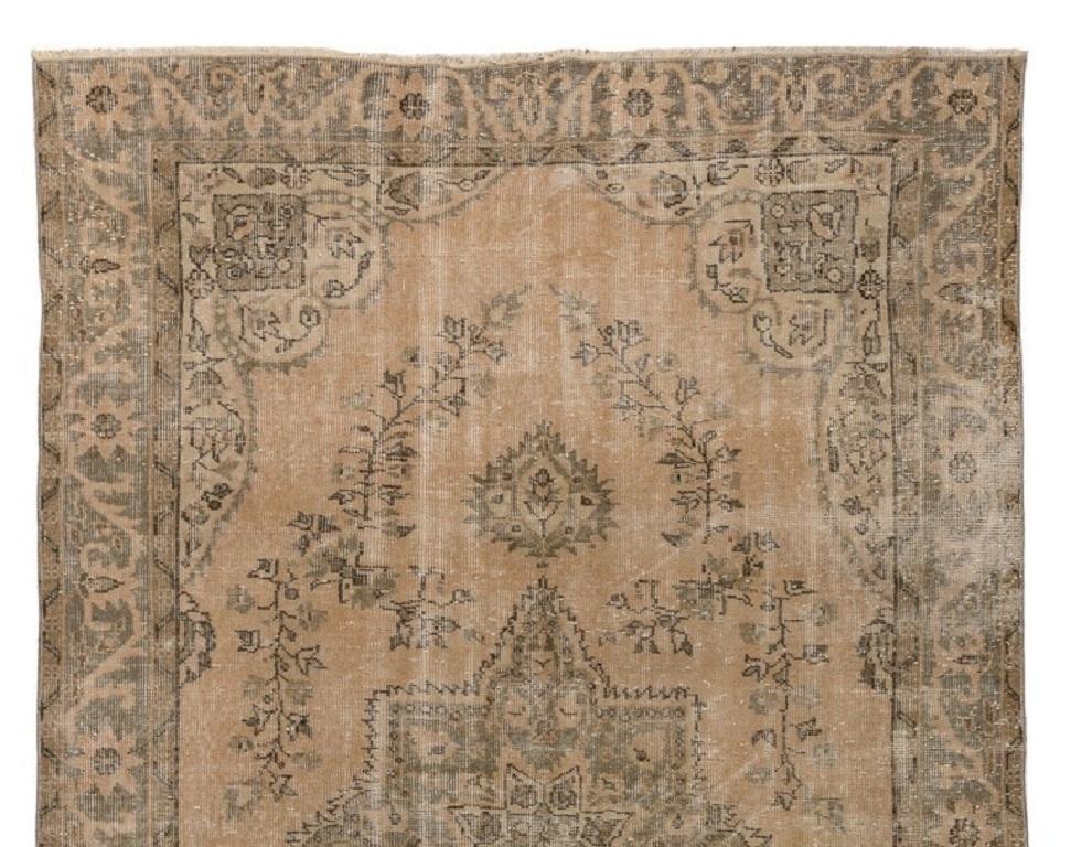 A vintage handmade and distressed Turkish area rug hand-knotted in the 1960s featuring a well-drawn central medallion decorated all around with scrolling floral vines in sage green against a golden sand background. The rug is finely hand-knotted