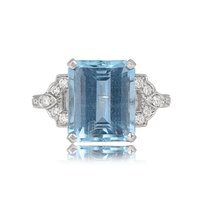 An 18k white gold ring showcasing a 5.80-carat emerald-cut aquamarine held in prongs. Geometric shoulders adorned with round brilliant diamonds lead to a diamond-set shank. The open-work under-gallery adds an elegant touch to this piece.

Ring Size:
