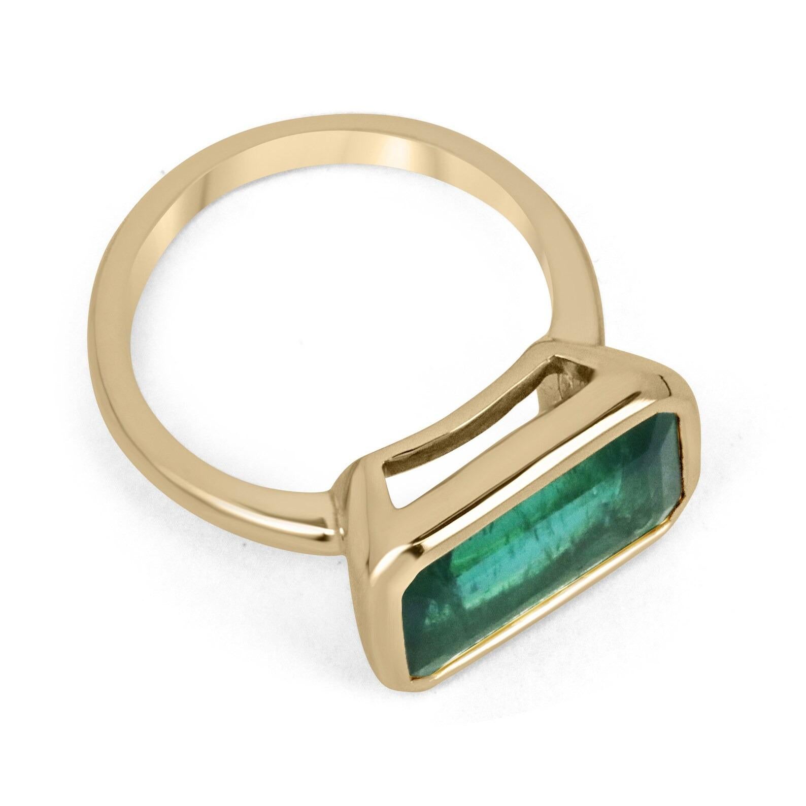 Displayed is a stunning East-to-West high-quality rare emerald solitaire engagement or right-hand ring in solid 18K yellow gold. This gorgeous solitaire ring carries a 5.48-carat emerald in a bezel setting. Fully faceted, this gemstone showcases