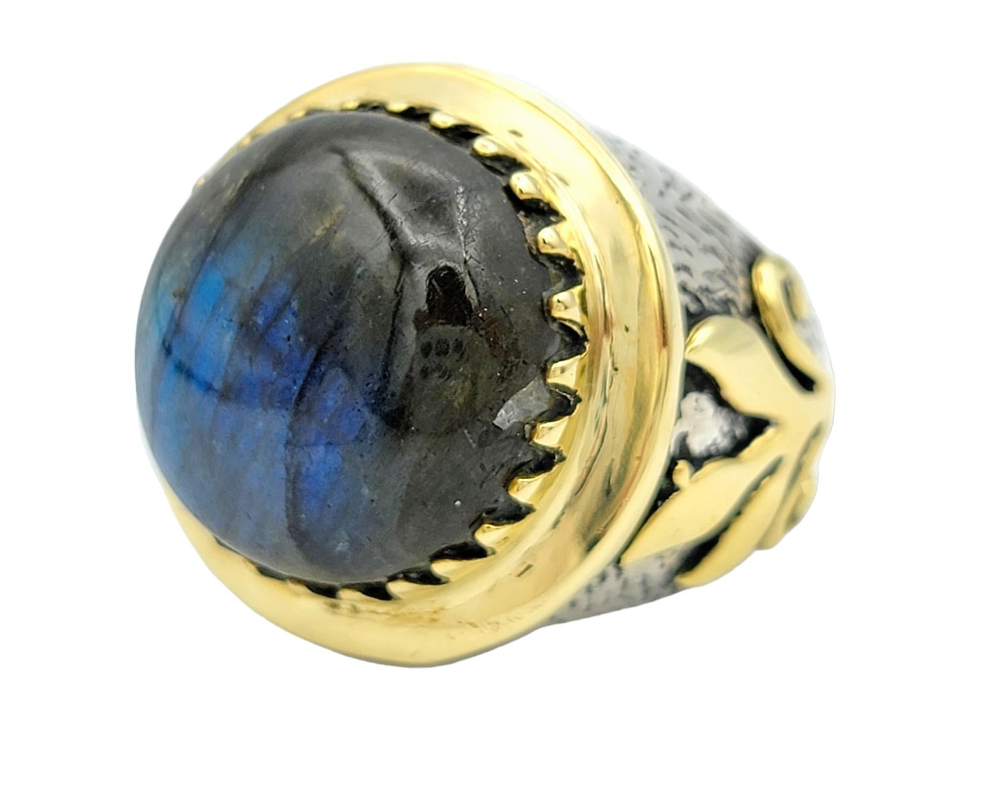 Ring Size: 8.5 

This unique cocktail ring is a striking and distinctive accessory that seamlessly blends bold design with sophisticated materials. The focal point of the ring is a commanding round labradorite cabochon, set with a unique prong