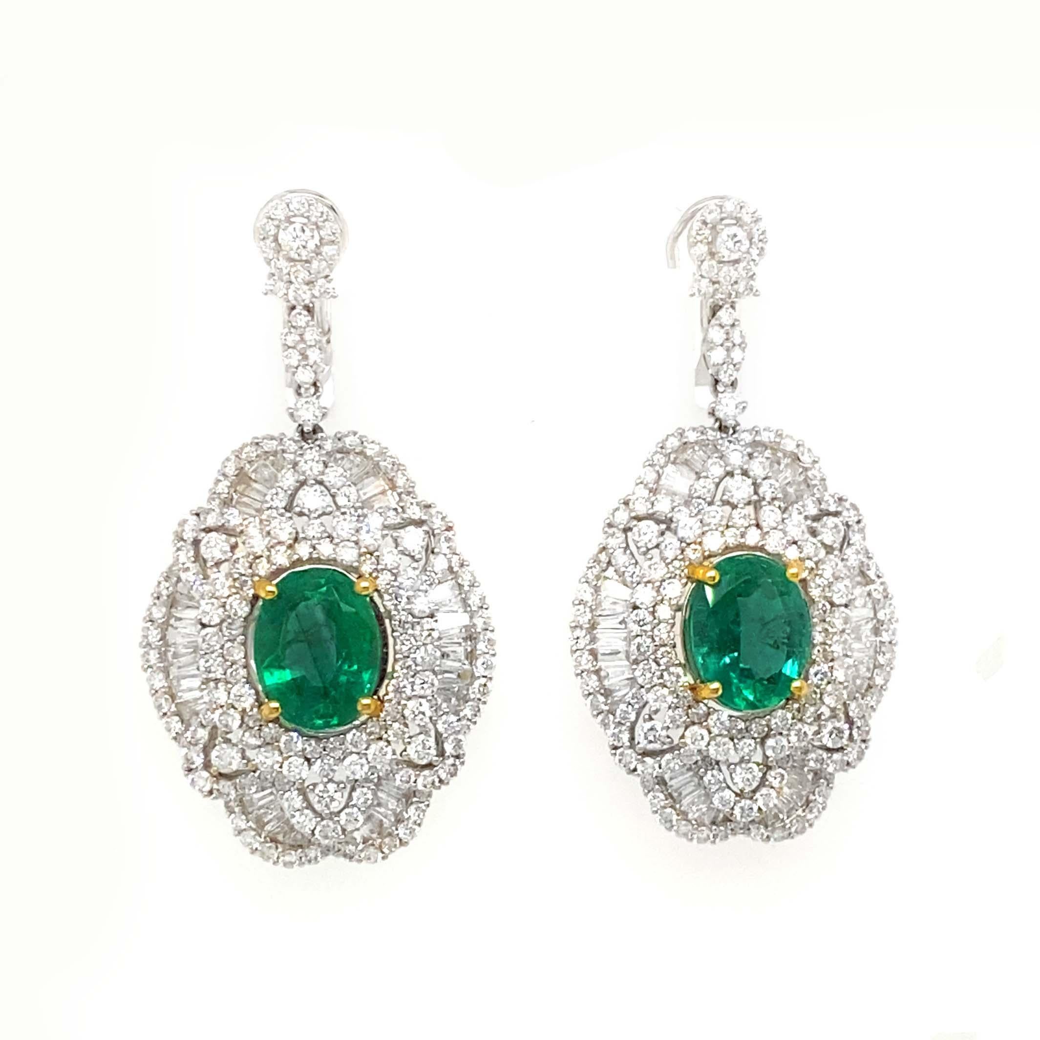 Round cut diamond earring studs drop to a beautifully designed cluster of diamonds with emeralds adorning the center. The main oval of the earrings includes a baguette and round cut diamonds. They surround the center which is a beautiful oval