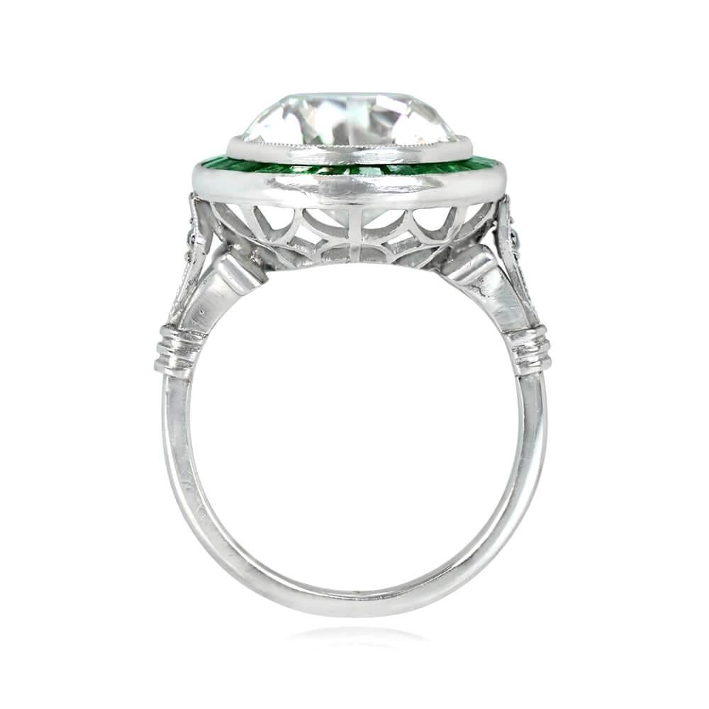 This engagement ring boasts a 5.91 carat old European cut diamond in K color and VS1 clarity, surrounded by a halo of 1.00 carat natural calibre-cut emeralds and milgrain detailing. The shoulders are decorated with diamond-shaped bezels set with
