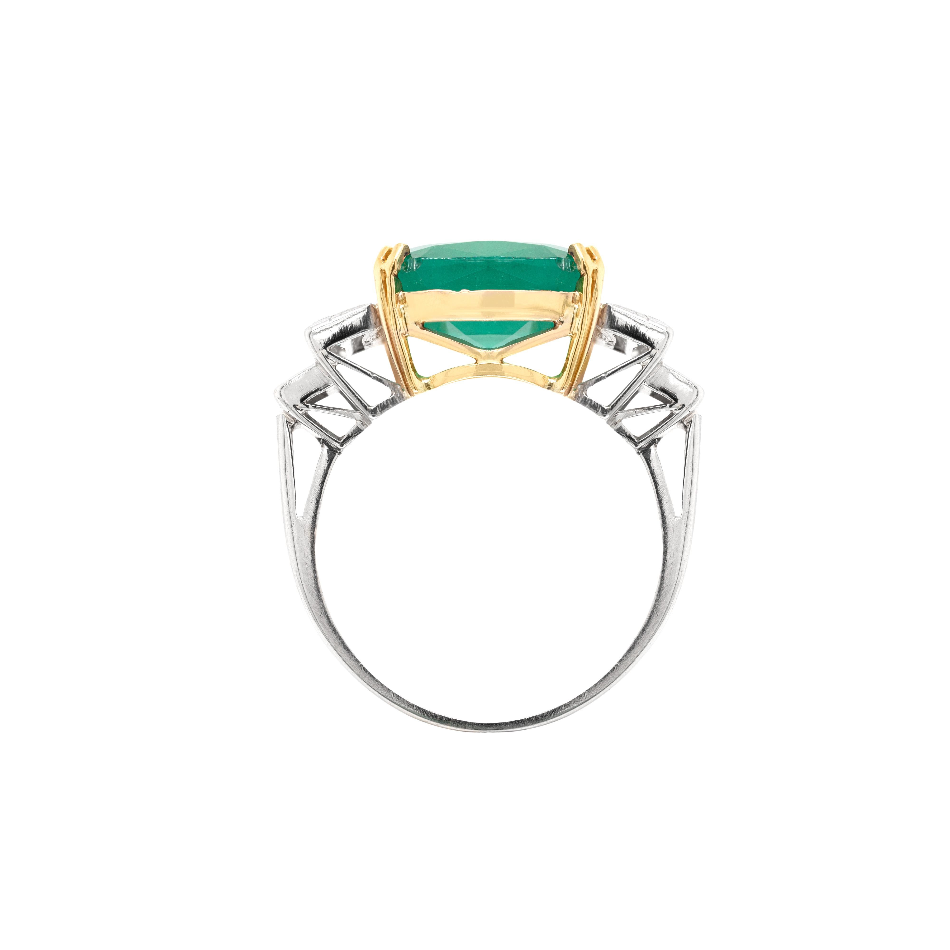 This wonderful engagement ring features an impressive 5.94ct cushion cut emerald mounted in a four double claw 18 carat yellow gold collet. The emerald is beautifully accompanied by two baguette cut diamond steps on either side with an approximate