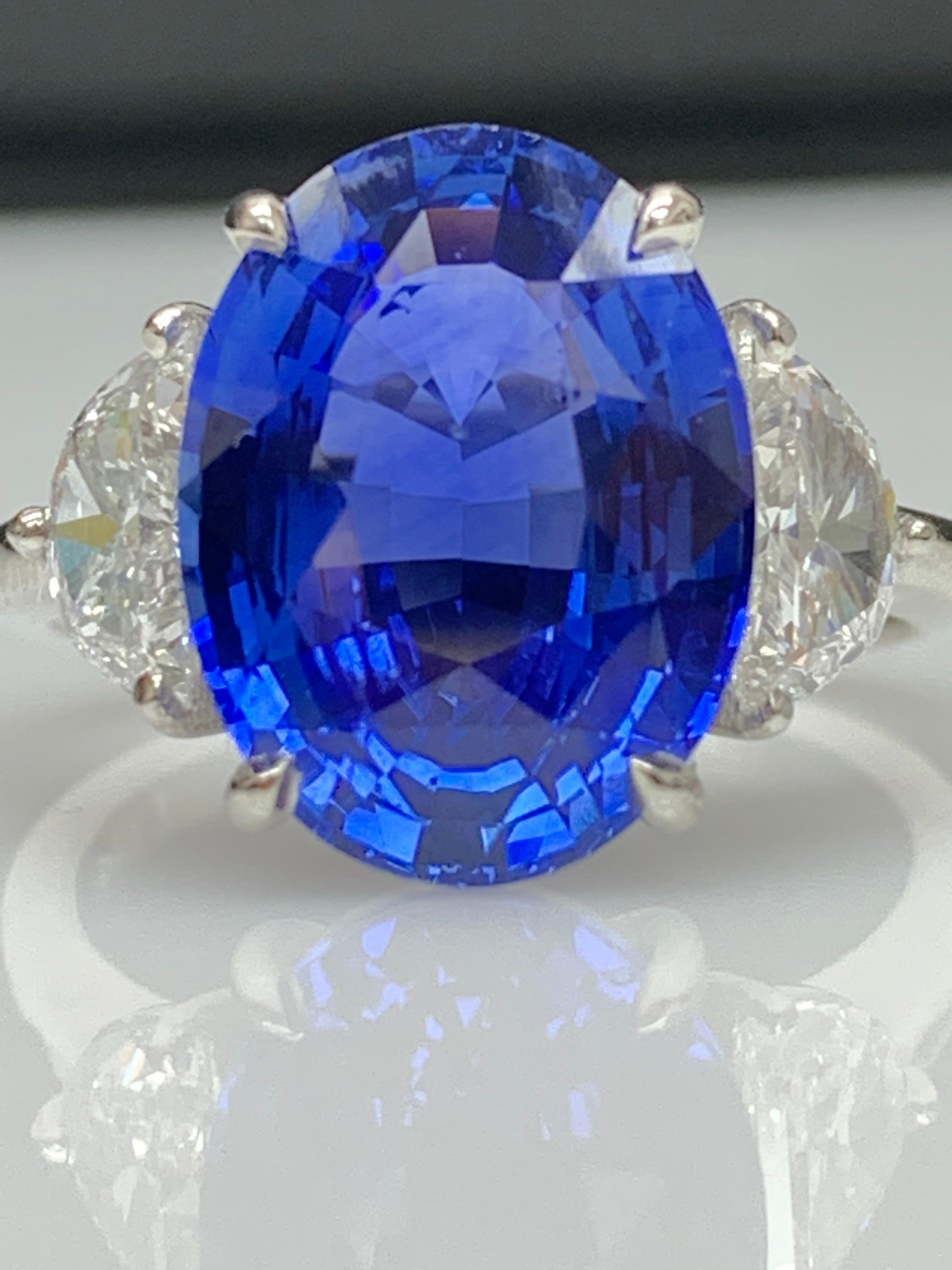 Showcases a Oval cut, Vibrant color Blue Sapphire weighing 5.96 carats, flanked by two brilliant cut half moon diamonds weighing 0.79 carats total. Elegantly set in a polished platinum composition.