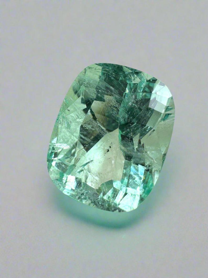 Stone: Emerald
Weight: 5.96-carats
Shape: Cushion Cut
Clarity: Transparent
Luster: Excellent-Very Good
Color: Light Green
Measurements: 12.60mm x 10.09mm x 7.98mm
Geographic Origin: Colombia
Treatment: Natural, Oiling

Comments: Due to their growth