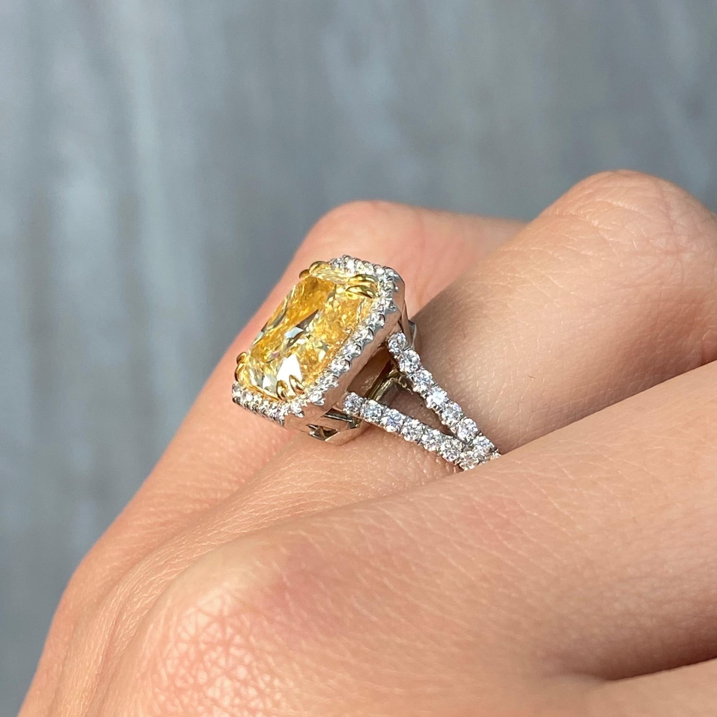 This elegant 5.01 carat light yellow diamond ring features a beautifully elongated radiant cut in the Y-Z color range, offering a soft, warm glow with exceptional brilliance. With VS2 clarity, the center stone is complemented by 0.79 carats of white
