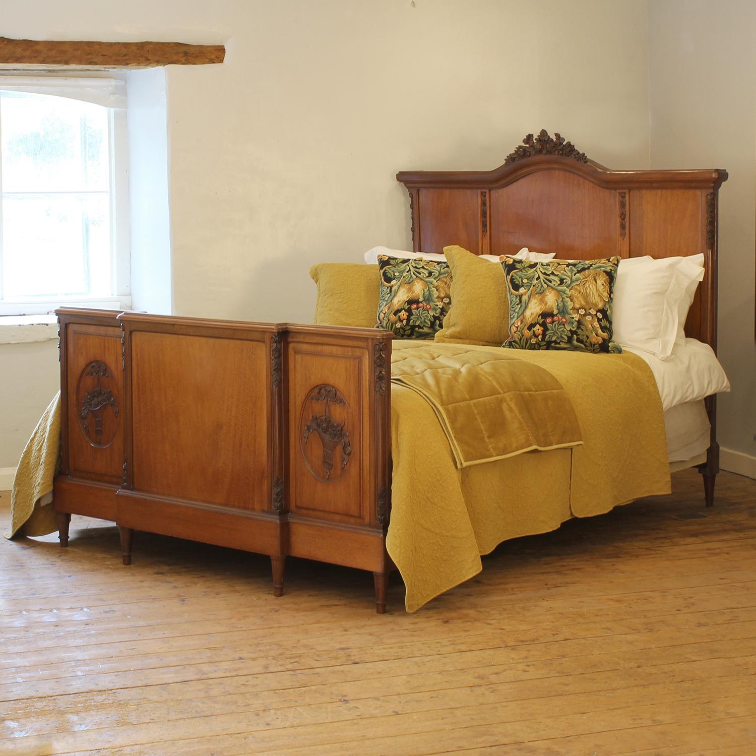 An elegant and wide Edwardian antique bed with carved panels on the footboard depicting baskets of flowers and a carved pediments on the headboards of a garland of roses. Both the headboard and footboard are divided into three panels with carved