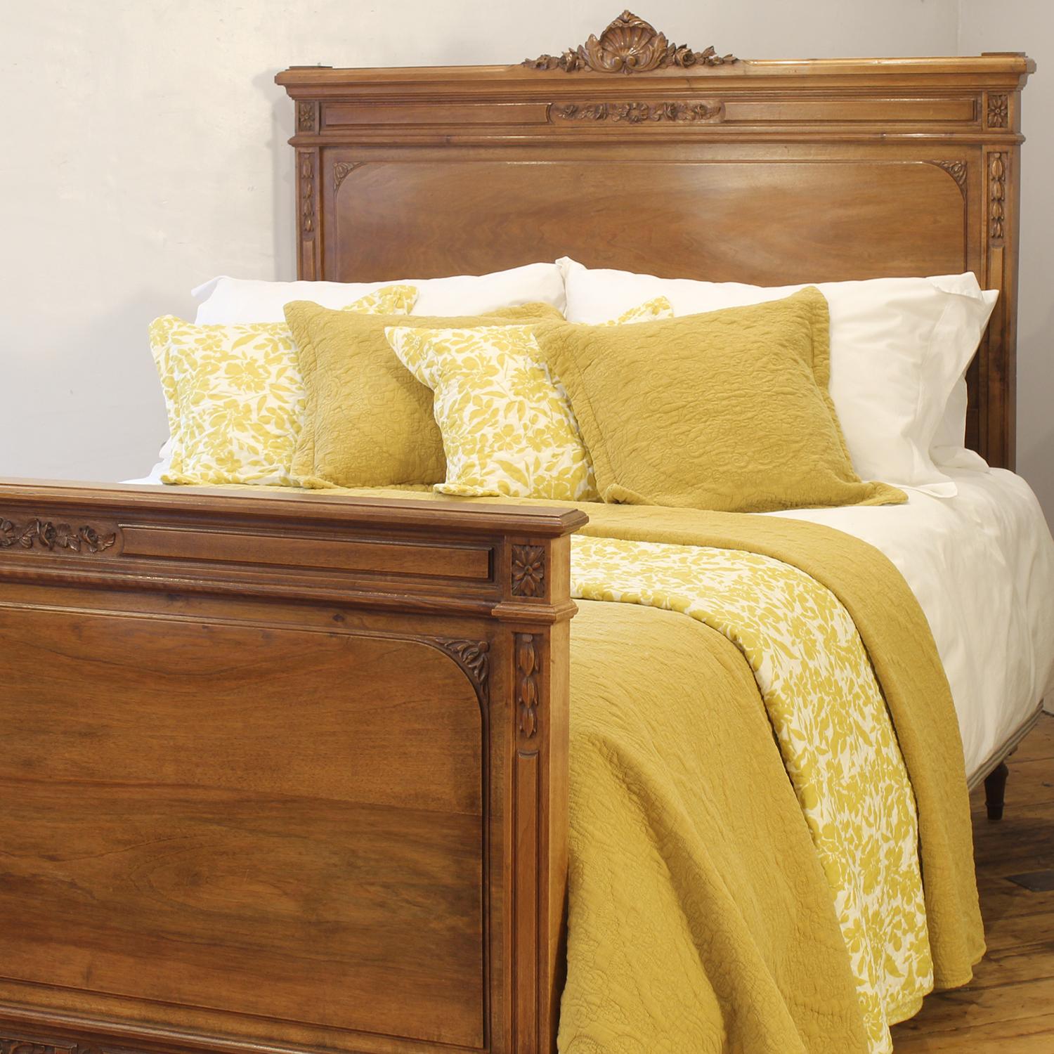 An elegant and wide Edwardian walnut antique bed. The bed is covered by hand carvings with a floral type design, topped off by a hand carved centrepiece on the headboard. The bed has straight edges with hand carved lines running down the sides of