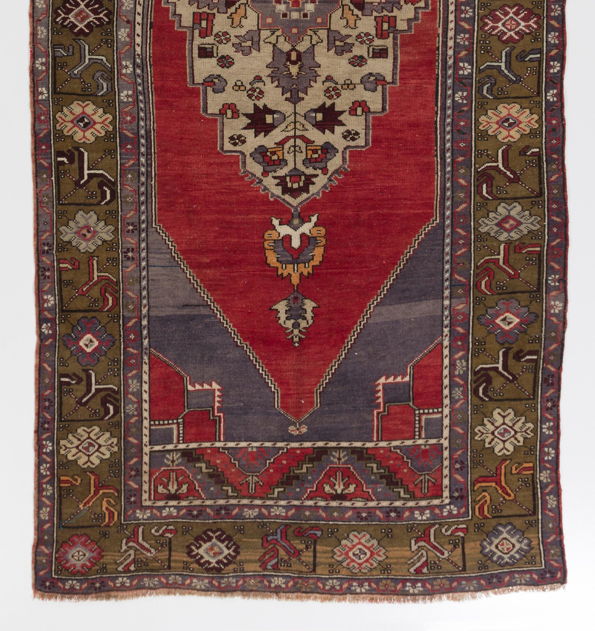 This vintage hand knotted Turkish runner rug features a large, elongated medallion in beige filled with geometric floral motifs at the centre of its plain red field. The corner pieces are in cerulean blue and feature striated color technique. The