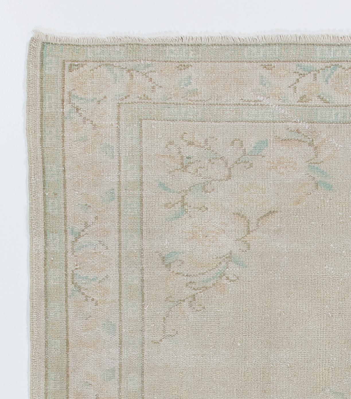 A finely hand-knotted vintage Turkish carpet from 1960s featuring a design inspired by Art Deco Chinese style with soft contoured floral motifs in neutral, pastel tones of golden sand and light aqua green, filling in the border, the corners of the