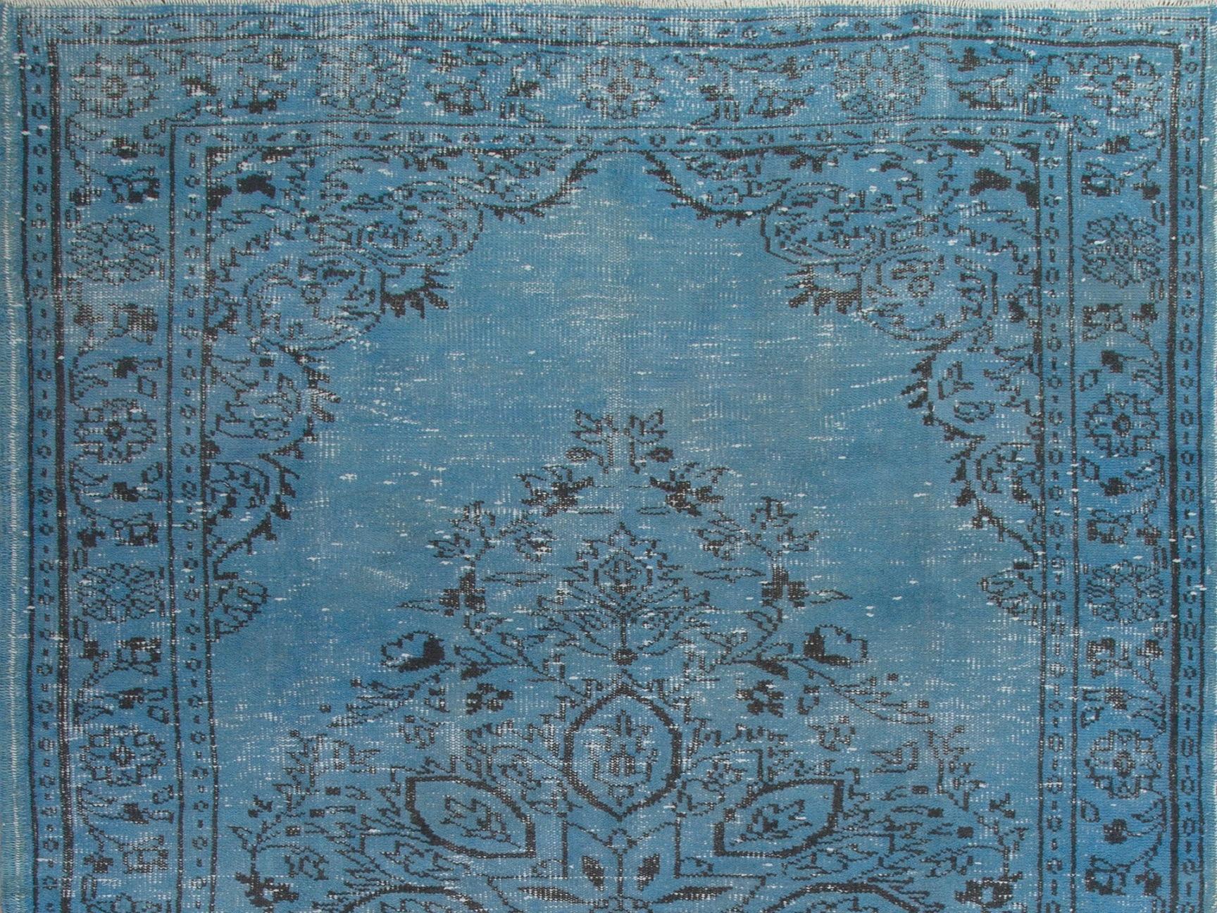 This hand knotted Turkish rug was originally made in the 1960s. It is over-dyed in vivid cerulean blue. It features a large floral medallion at the centre against a plain field, arabesque corner pieces and a main border decorated with floral heads