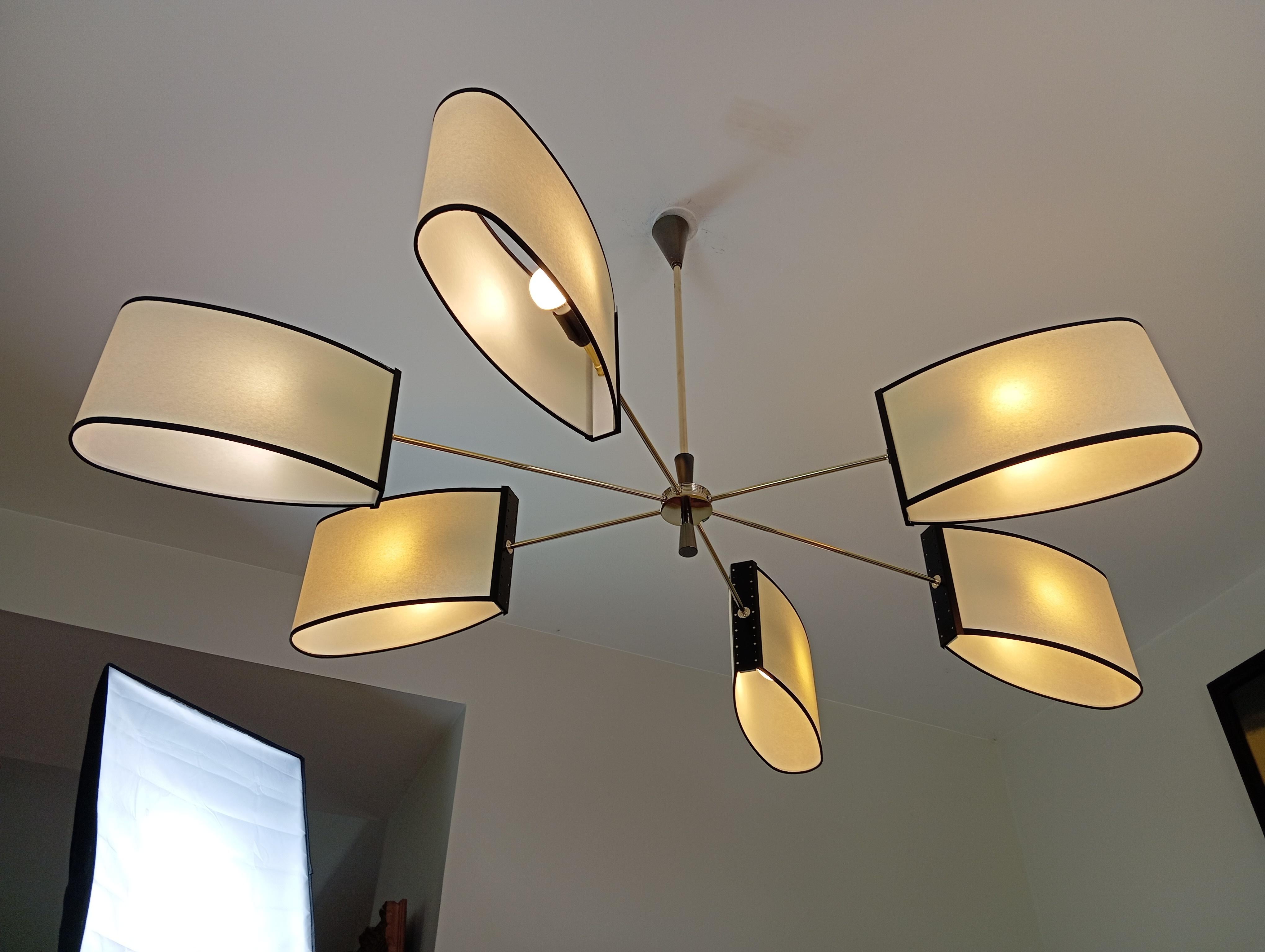 Brass and black lacquered metal chandelier, of asymmetrical form, composed of a cylindrical brass base, adorned with conical shapes in gun patina brass, and 6 brass arms supporting oval shades.
This chandelier has been restored, the wiring rewired