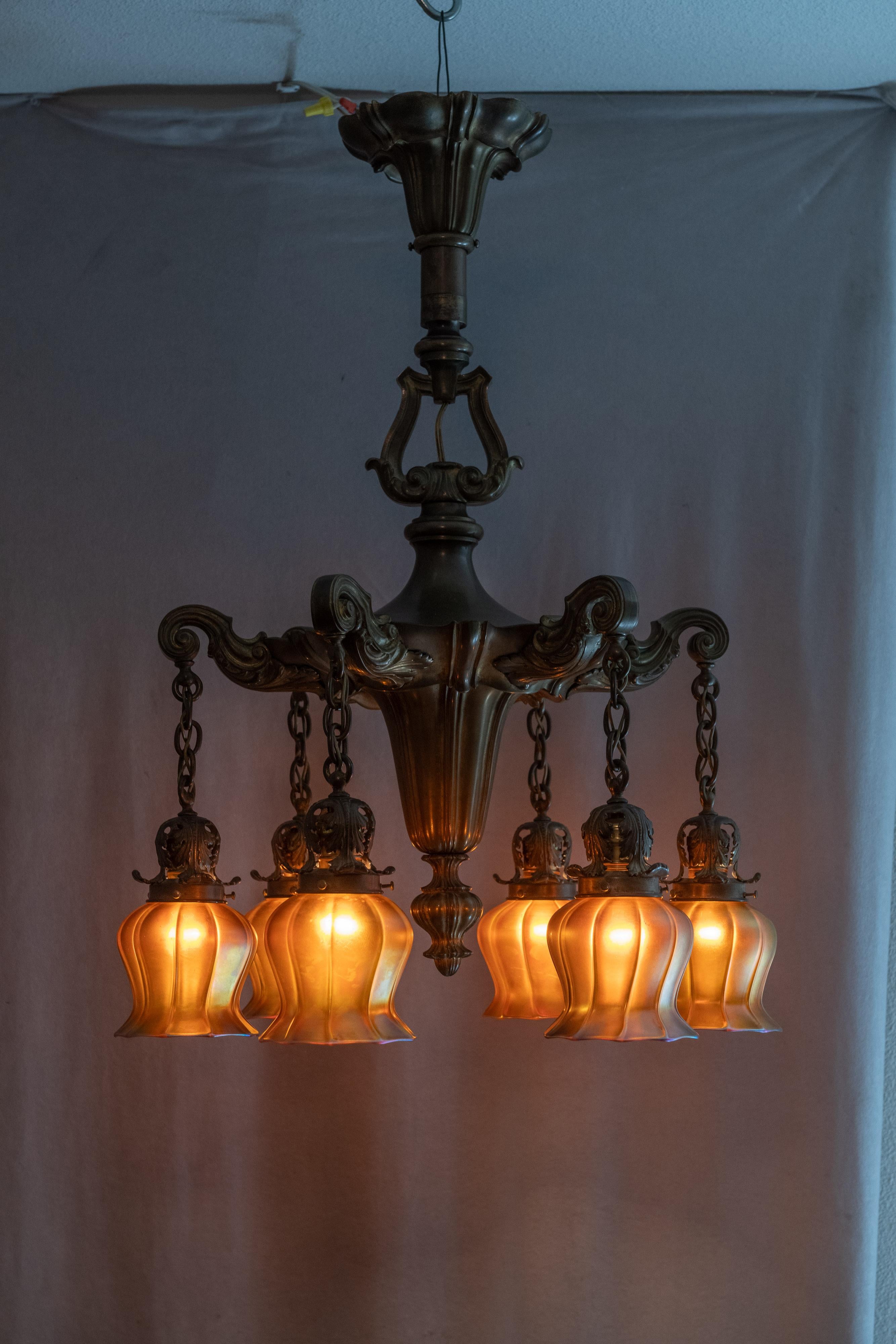 This chandelier is a high quality piece of lighting. Cast in bronze with the original lovely factory patina. Even the ceiling canopy is cast bronze. The hand blown art glass shades all match and are signed by Quezal, one of the most important and