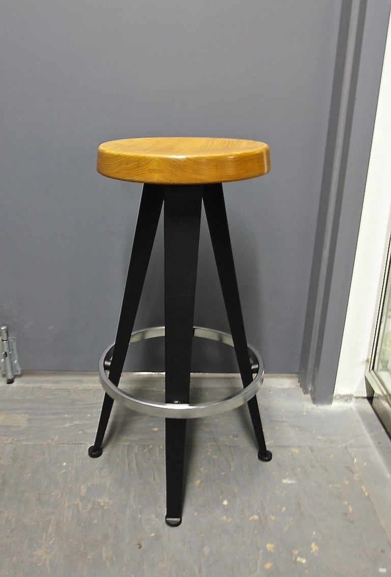 Six bar stools in black enameled metal, a brushed aluminum footrest, and a seat in hand-turned, stained oak with a slight concave in the center.
They are an updated and improved version of Prouvé's 1952 design.