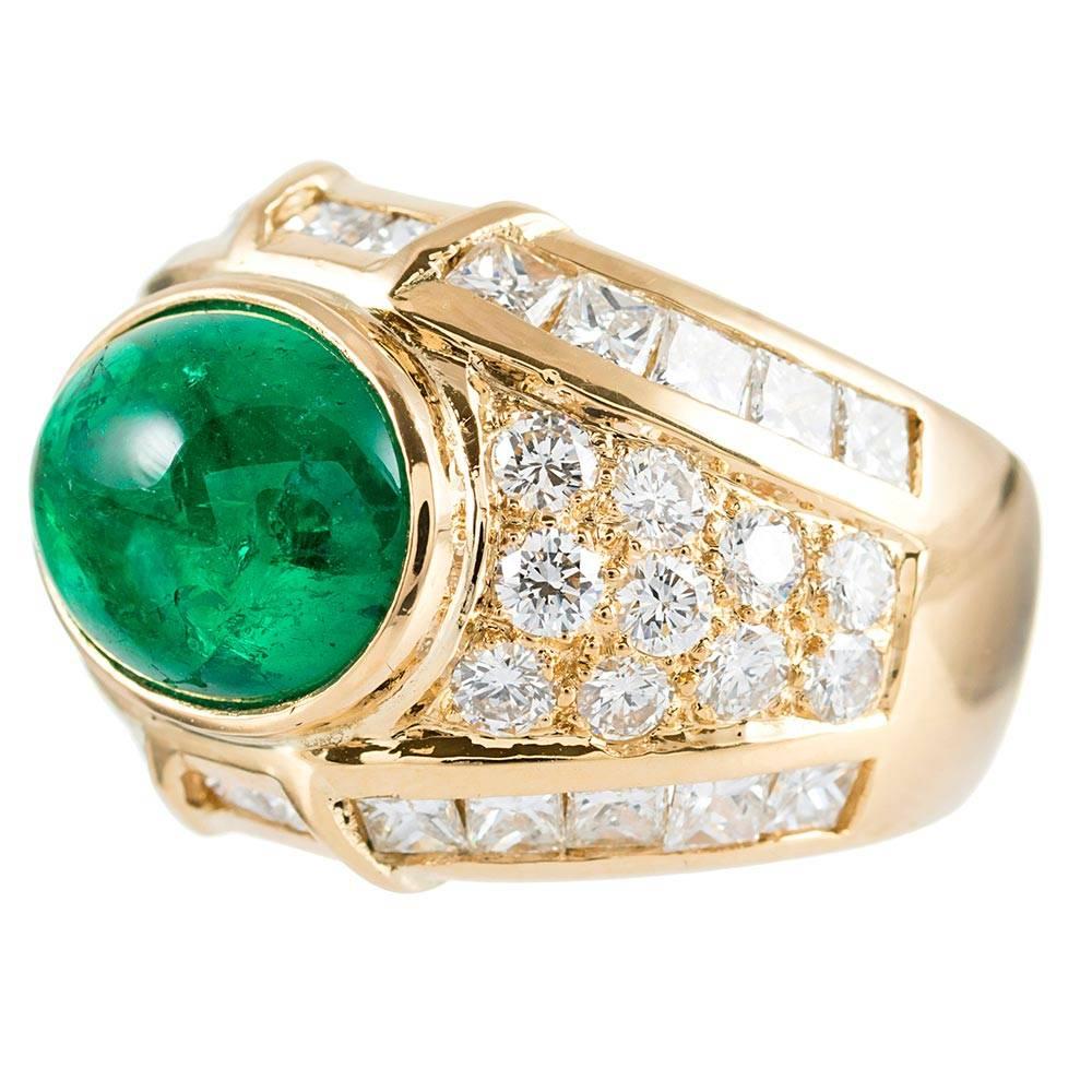 A fabulous likely 1980s or 1990s creation with an impressive presence, the center stone is a 6 carat cabochon of emerald flanked on all sides by mixed cuts of white diamonds that weigh 4.24 carats combined. The round and princess cut diamonds