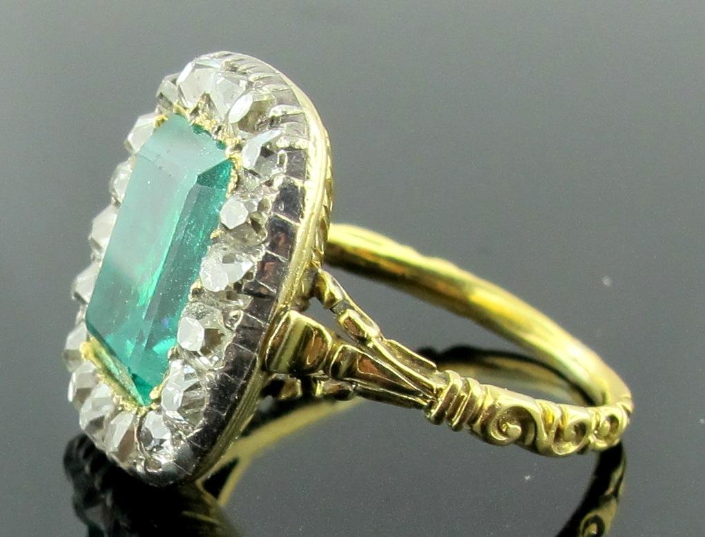 Circa 1880 6 carat emerald cut Emerald surrounded by 18 old mine cut diamonds with a weight of 1.10 carats.  Set in silver on 14 karat yellow gold. Ring size is 6