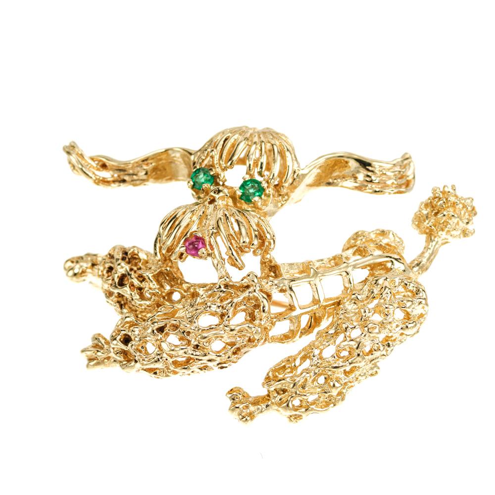 1950's Emerald and ruby yellow gold poodle brooch. 2 round emerald eyes approximately .6cts with a round cabochon red ruby mouth. 18k yellow gold. 

2 round green emeralds, approx. .6cts
1 round red cabochon ruby, approx. .3cts
18k yellow gold