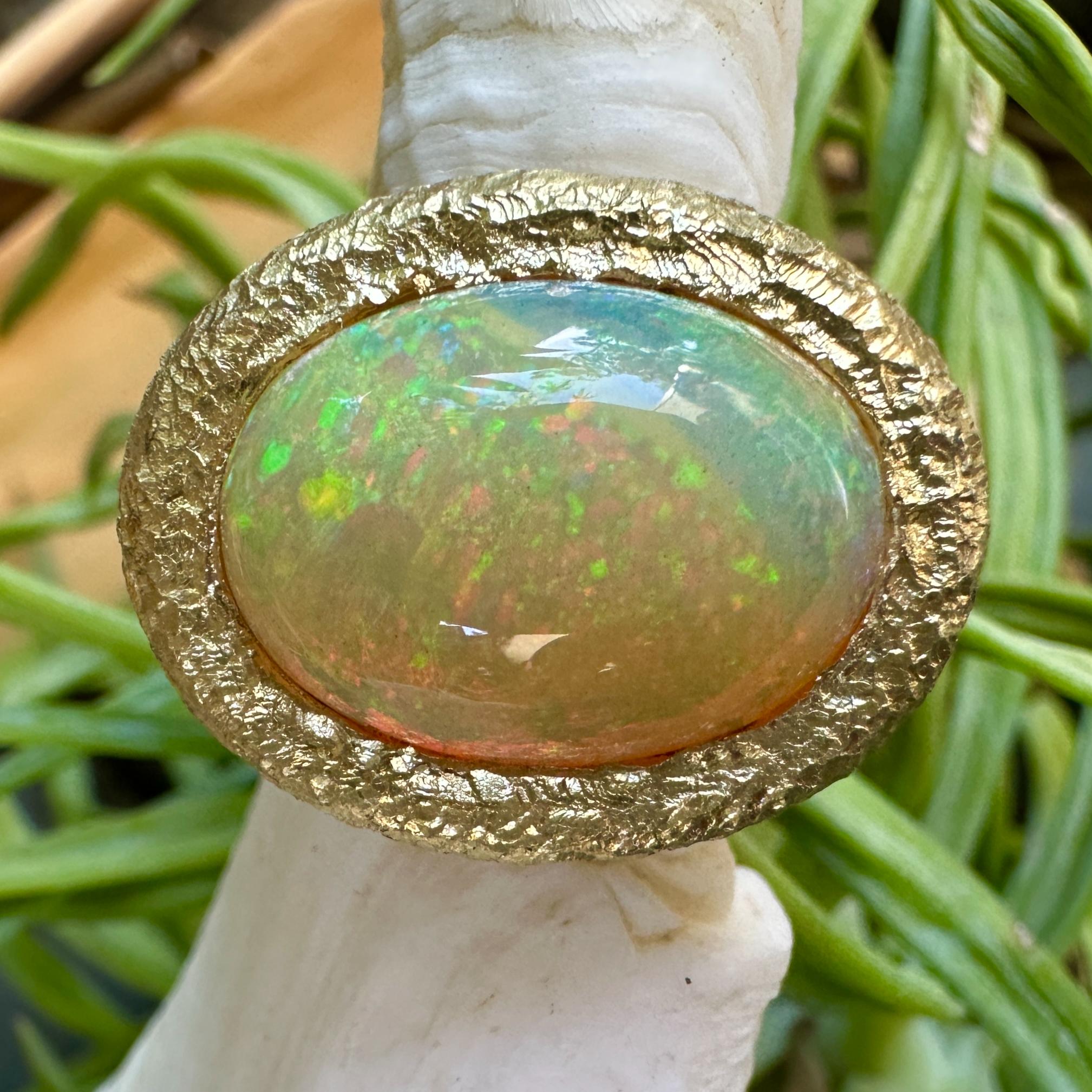 A gorgeous Ethiopian opal with yellow and blue body color shows fiery sparks of red and green and, like all good opals, looks different from every angle.  Eytan set it horizontally in a bezel ring with a thick outer rim of textured 18 karat gold. 