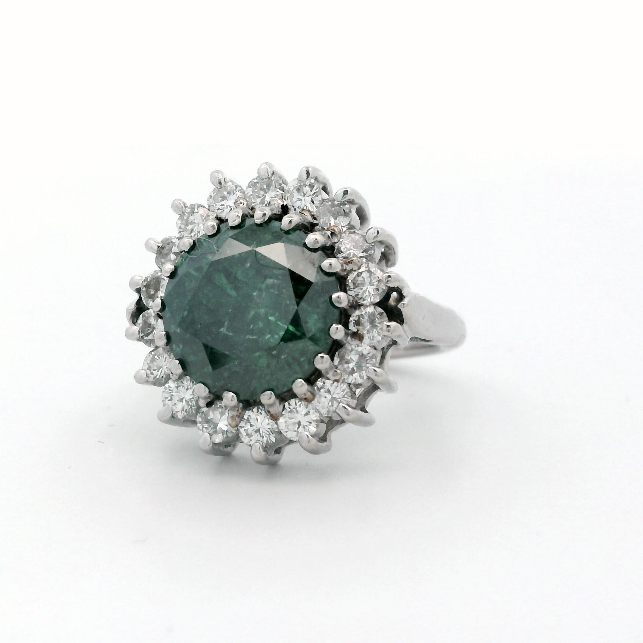 Un diamante verde único con un toque de azul presentado en un halo de diamantes de talla brillante redondos casi incoloros. El anillo está fabricado en oro blanco de 14 quilates y se expande para ajustarse a los nudillos. 