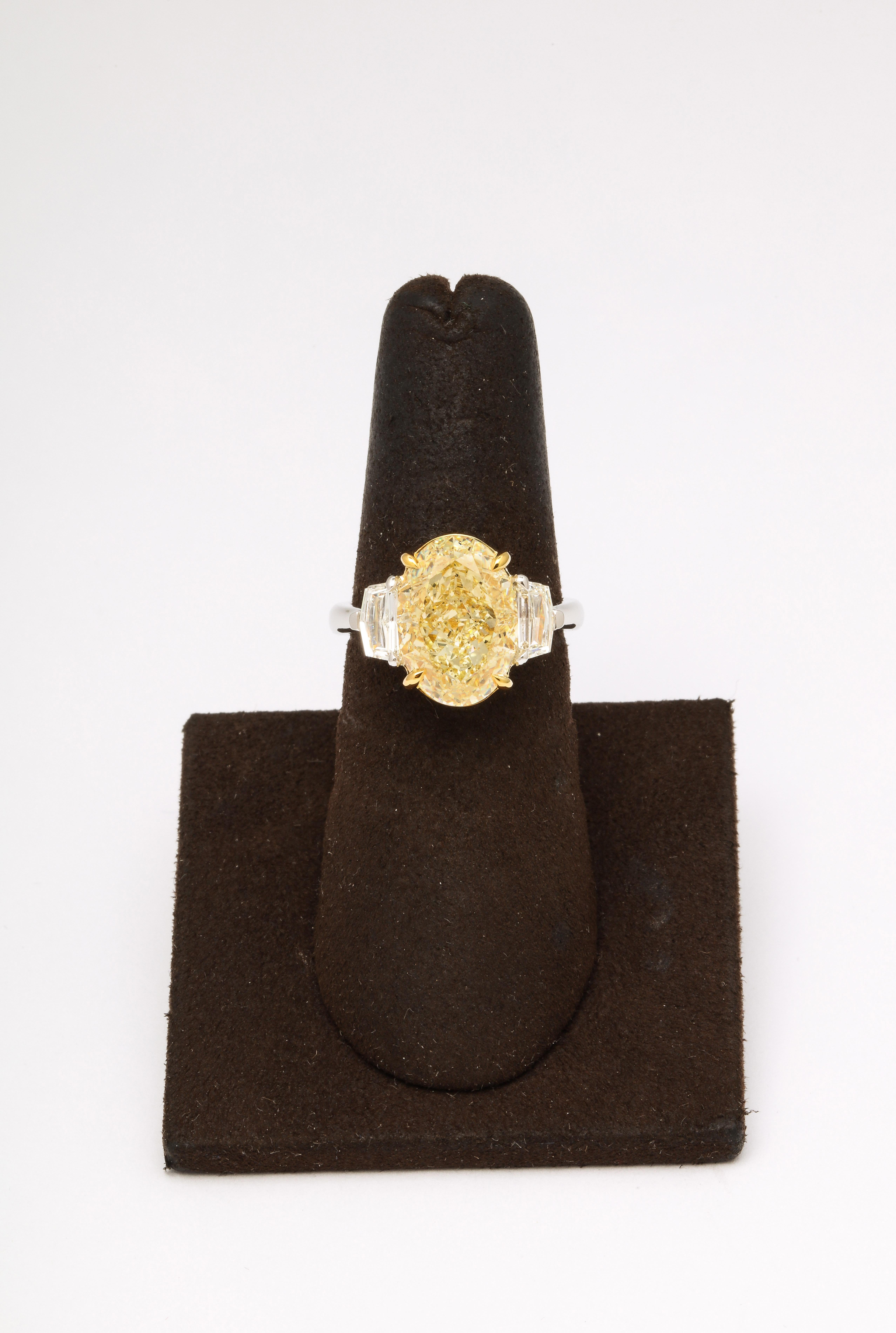 
6.03 carat GIA certified Fancy Light Yellow Oval center diamond, SI1. 

Ideal Oval shape - with strong deep yellow color - and lots of brilliance! 

.61 carats of epaulette white side diamonds. 

Custom made in 18k yellow gold and platinum.
