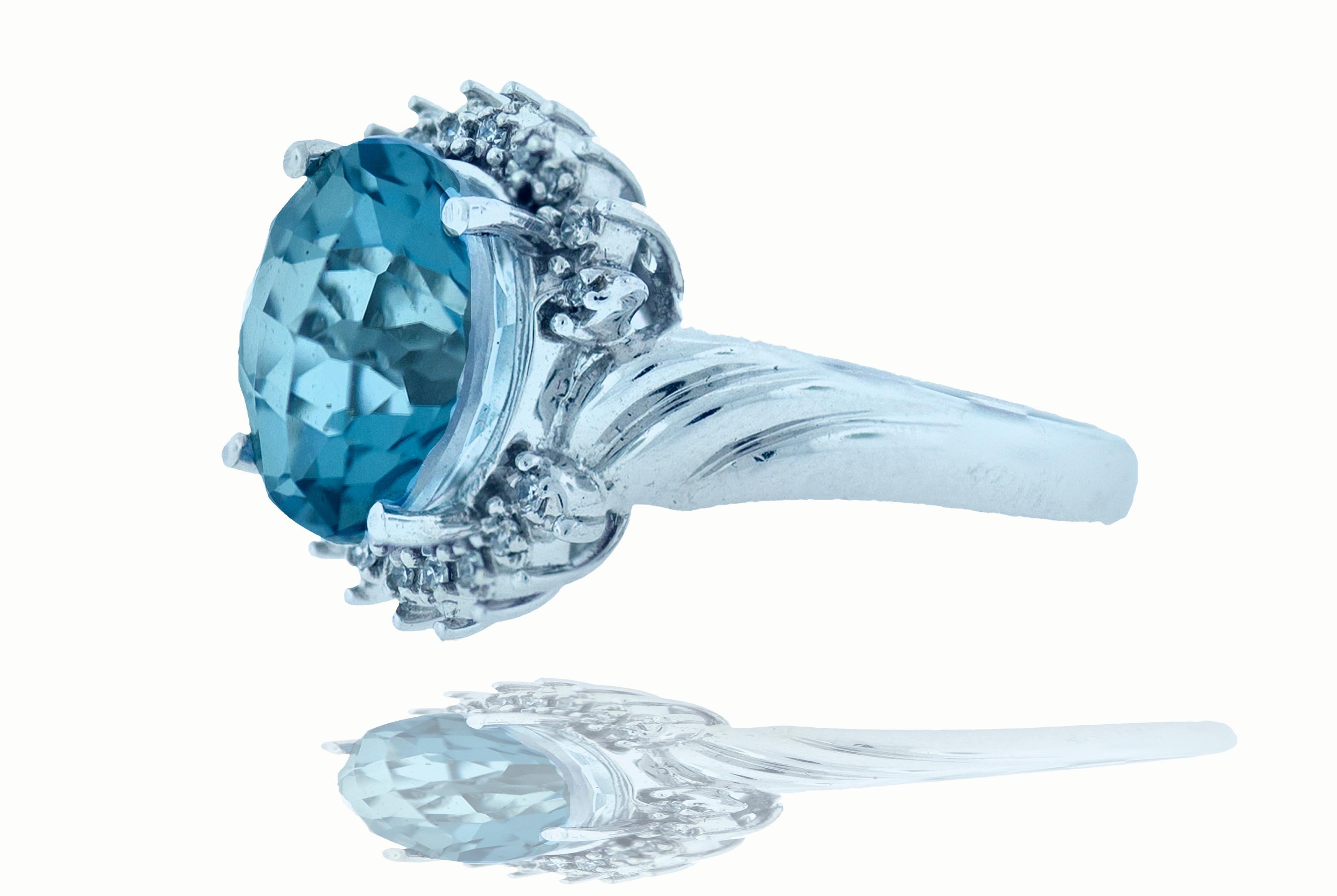 6.2 blue topaz cocktail ring with diamond halo. The center topaz of the ring measures 12.11 by 12.10 in a round cut. There are 18 - 1mm diamonds approximately .09 ctw that beautifully surrounding the center topaz. This fashion ring is set in 14k